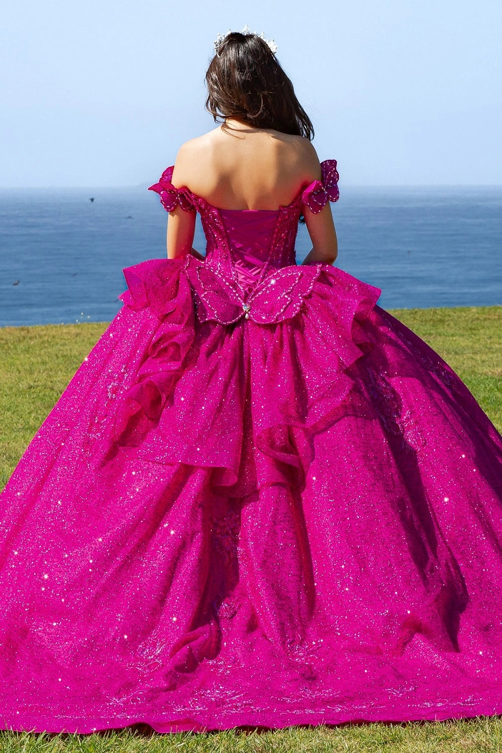 Displayed in a back detail, the Fuchsia quinceañera dress has lace-up back and a large butterfly bow above the layered skirt.