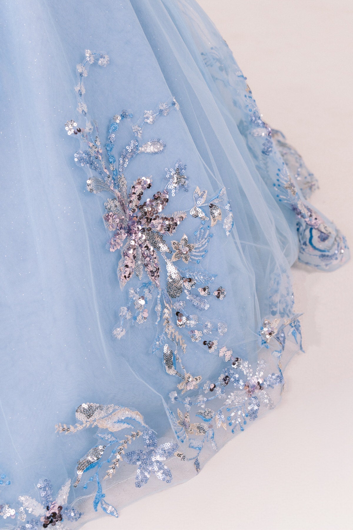 Light blue fabric close-up kids mini quinceañera mini quince dress with floral embroidery, sequins and glitter tulle.