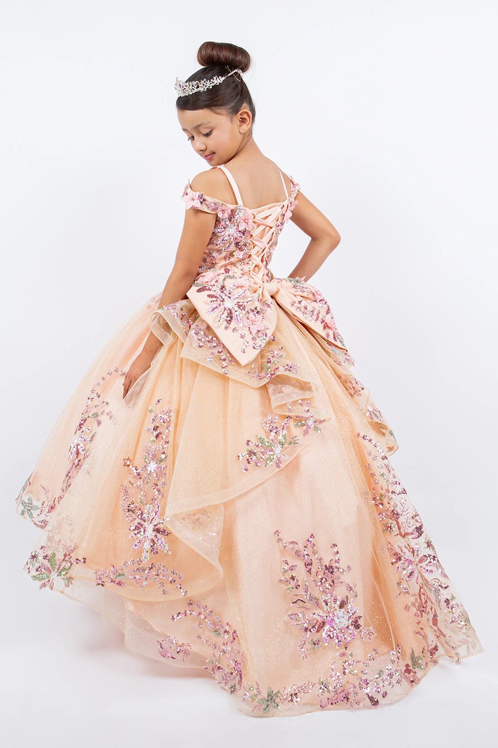 Displayed in a back view, the Peach Blush mini quince dress has lace-up back and floral bow above a tiered tulle skirt.