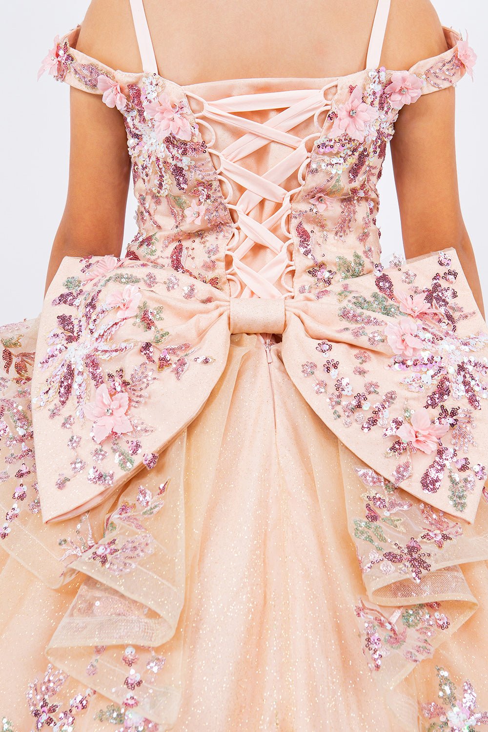 Close-up back view of a peach blush kids mini quince dress with 3D beaded floral applique glitter tulle with big bow.