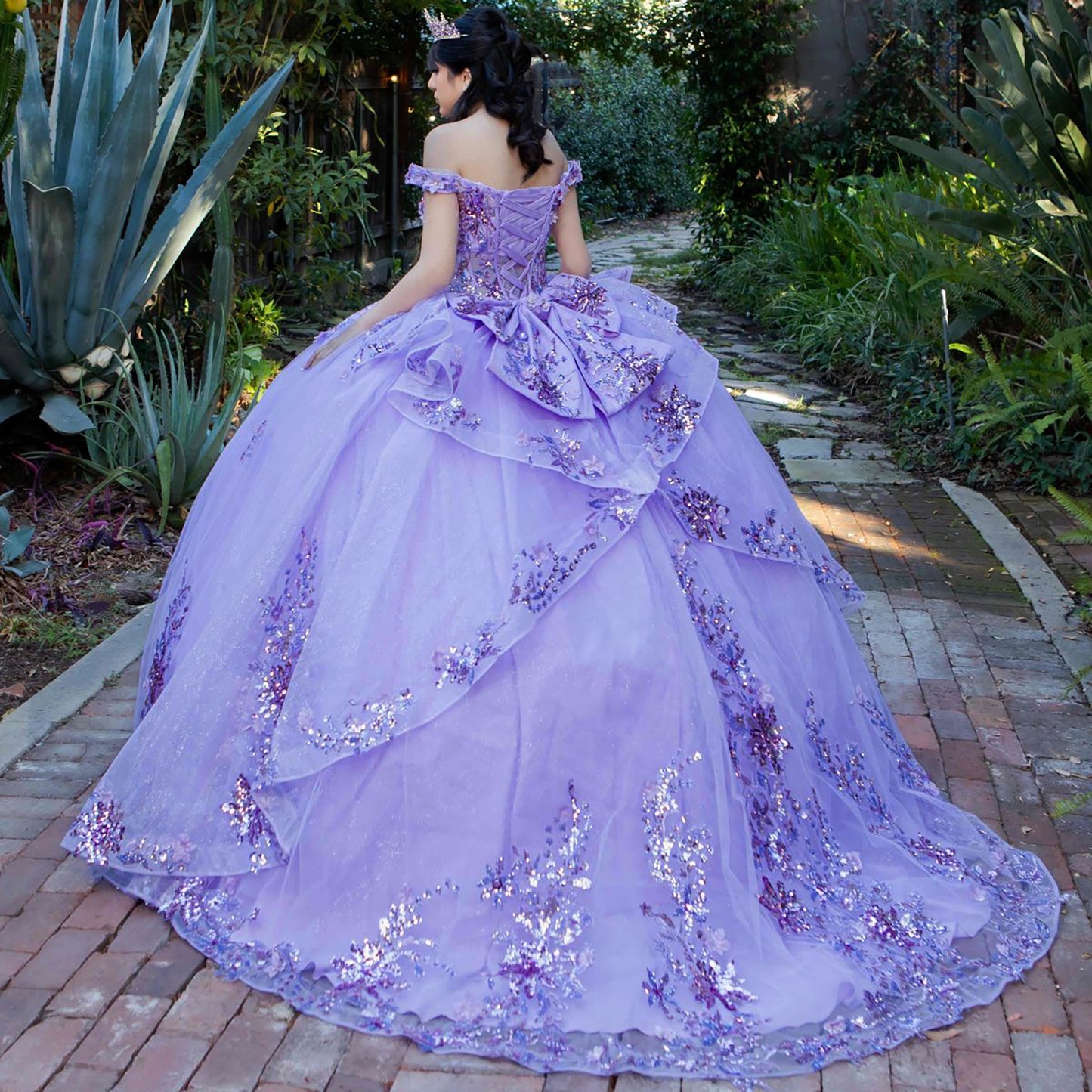 Back view of a woman wearing lilac quinceanera ball gown with seven-layer tulle skirt, floral beaded appliques, and lace-up train