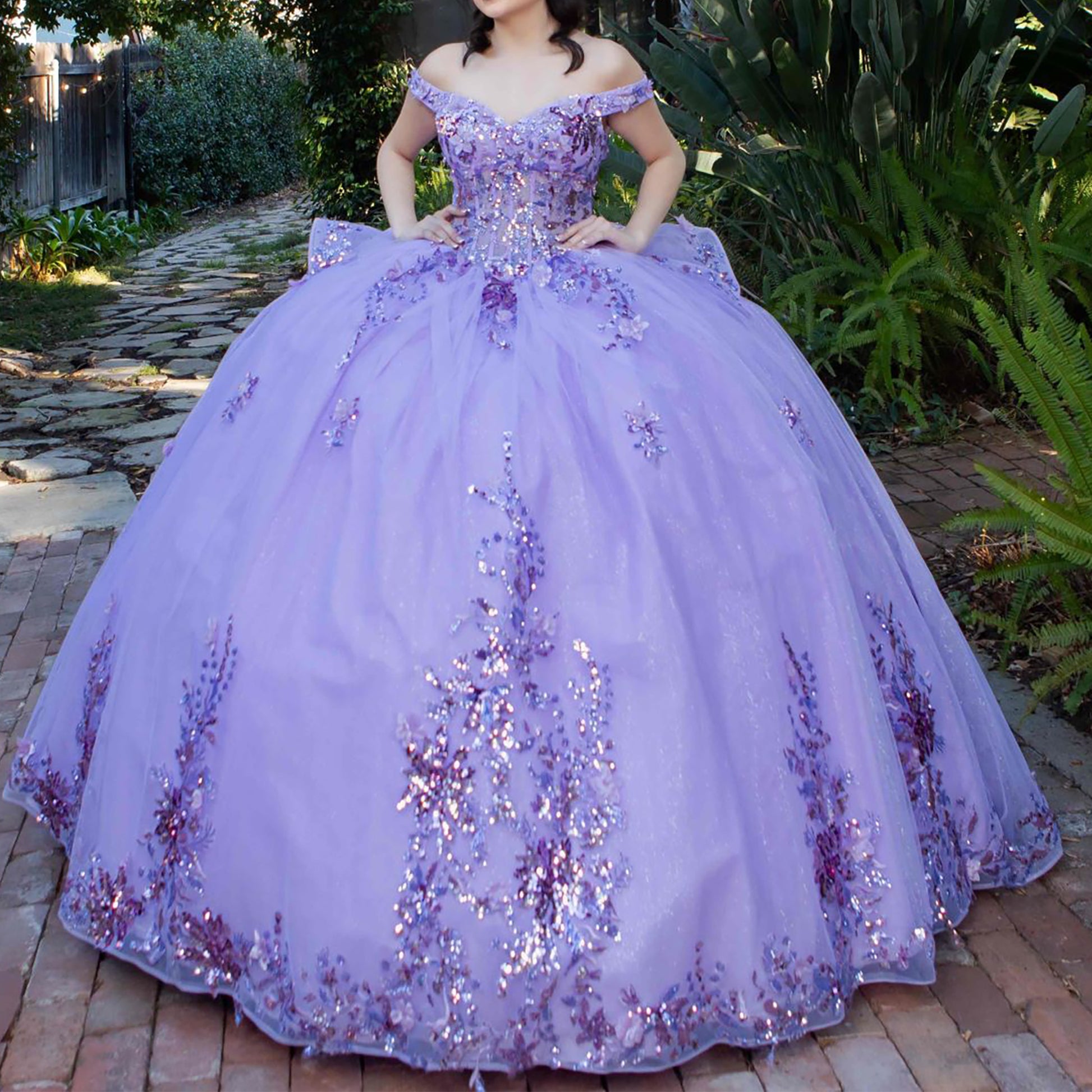 Full view of a woman wearing lilac quinceanera ball gown with seven-layer tulle skirt, floral beaded appliques, and sweep train