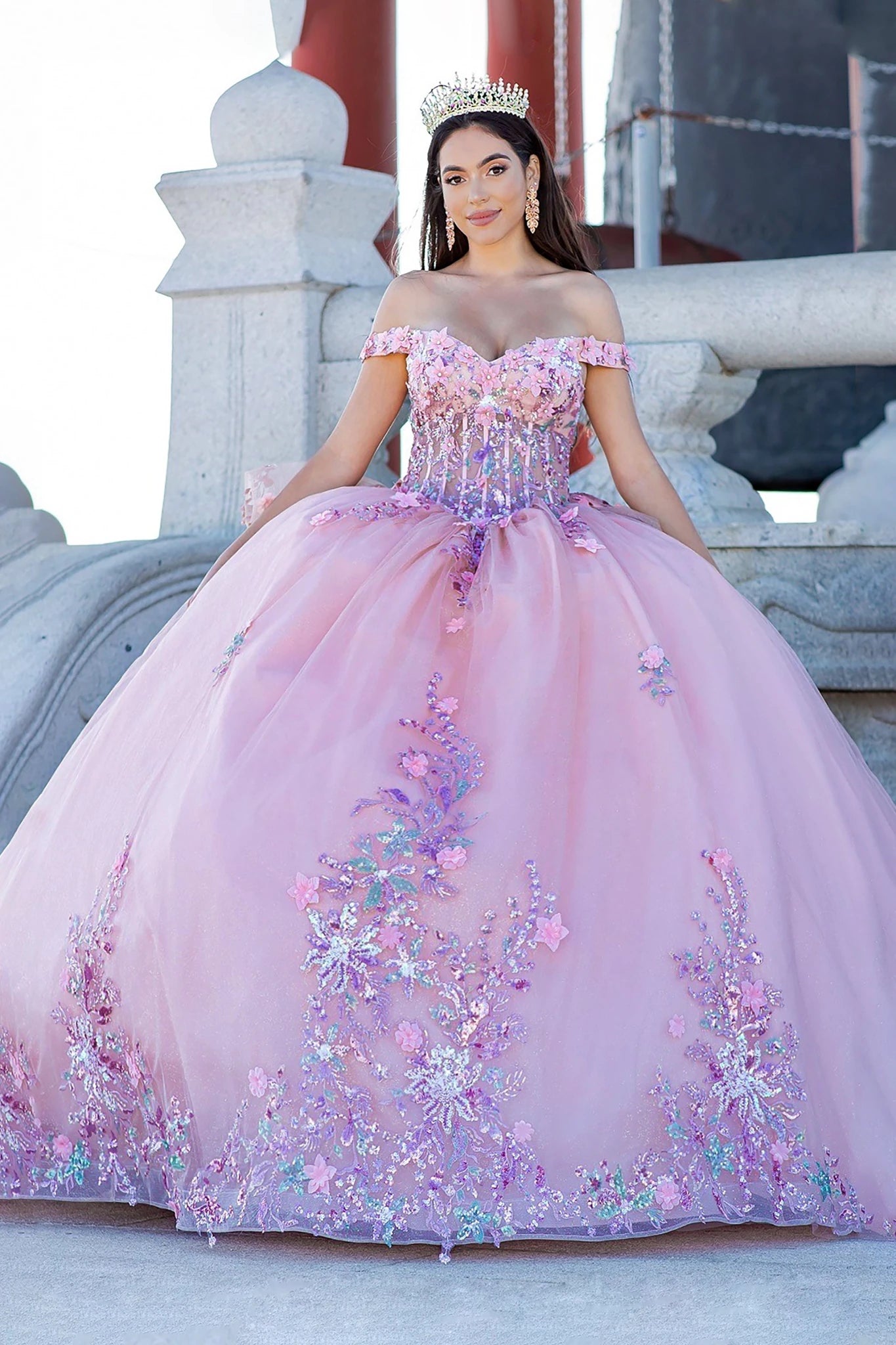 Front view of a woman wearing peach blush quinceanera ball gown with floral beaded appliques, layered tulle skirt, and tiara accent
