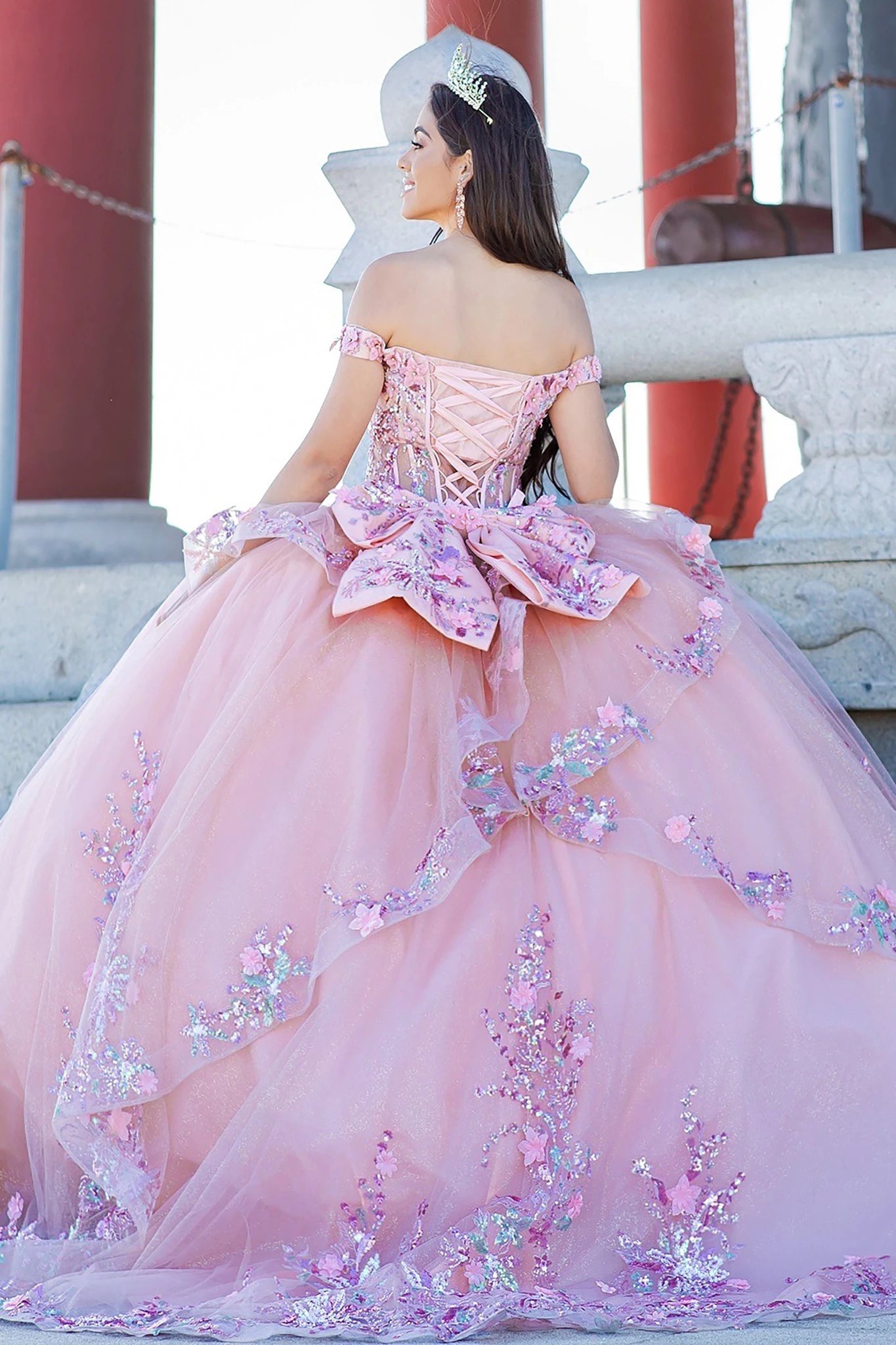 Front view of a woman wearing peach blush quinceanera ball gown with floral appliques, layered tulle skirt, and glitter detailing