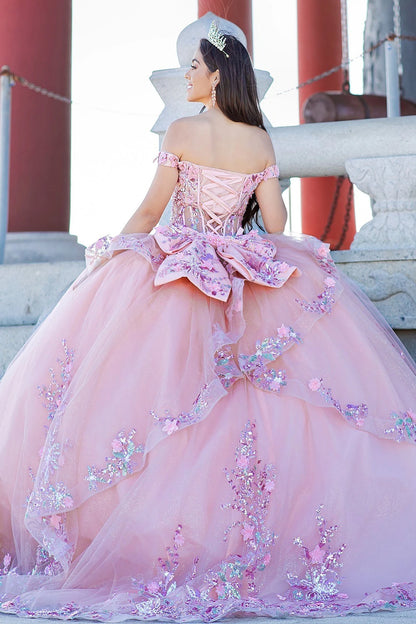 Front view of a woman wearing peach blush quinceanera ball gown with floral appliques, layered tulle skirt, and glitter detailing