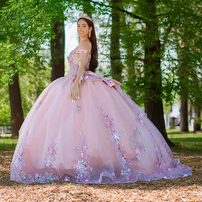Front view of a woman wearing peach blush quinceanera dress with floral appliques, layered tulle skirt, and outdoor background