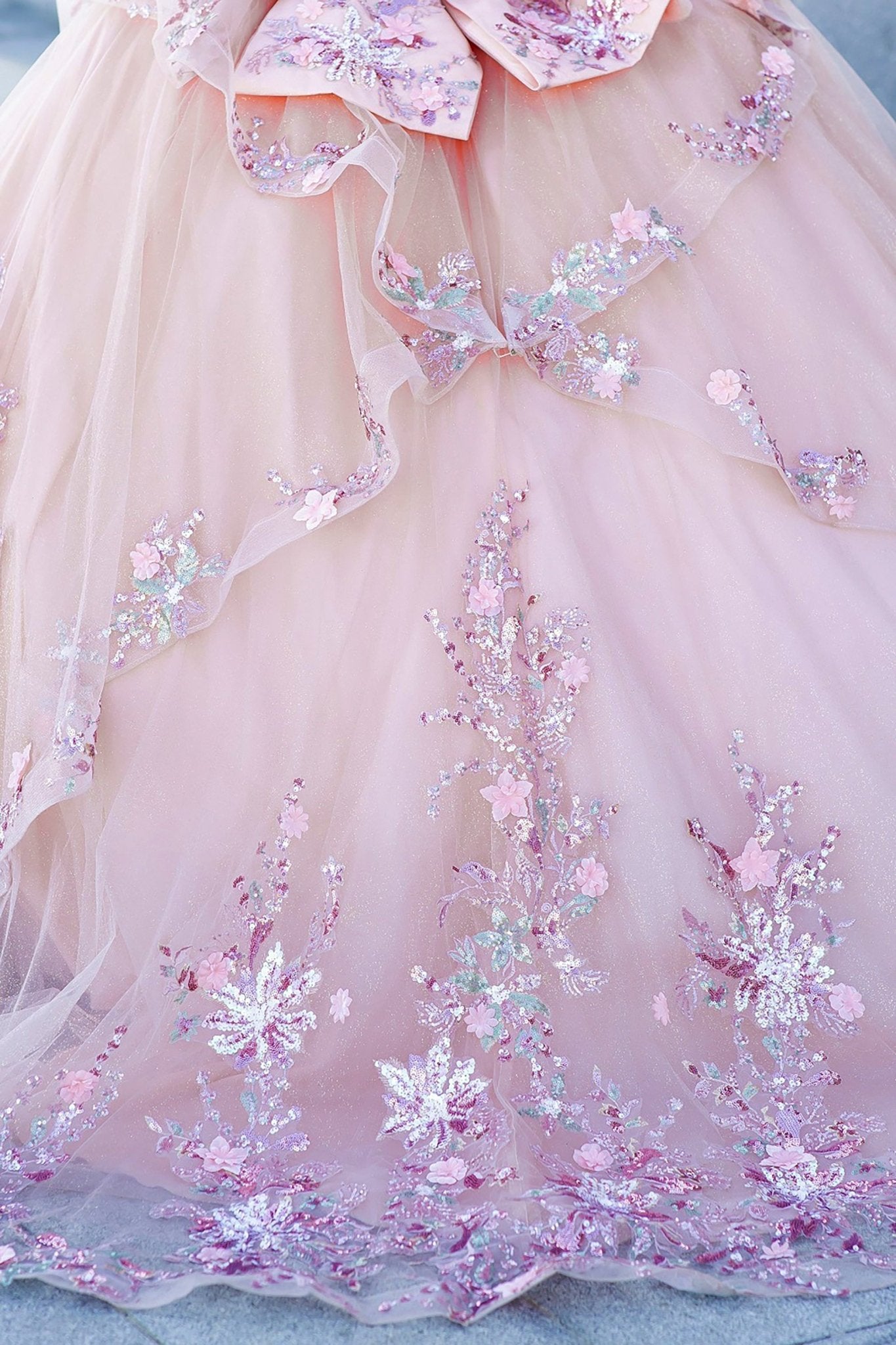 Front view of a woman wearing peach blush quinceanera ball gown with floral appliques, snowflake embellishments, and layered tulle skirt