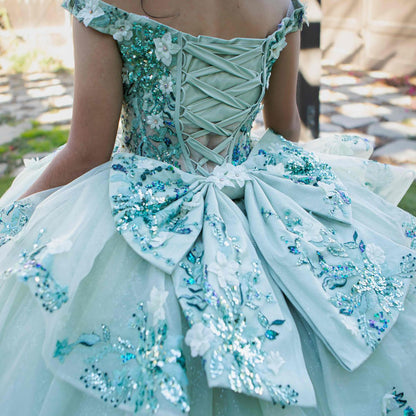 Back view of a woman wearing sage quinceanera ball gown with lace-up corset, floral beaded appliques, and seven-layer tulle skirt