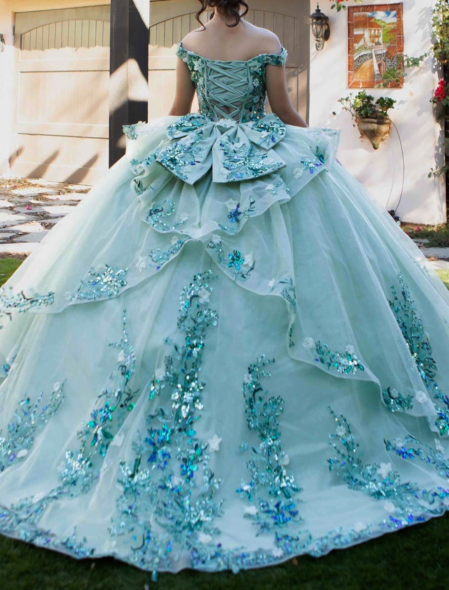 Back view of a woman wearing sage quinceanera ball gown with lace-up corset, oversized bow, and seven-layer tulle skirt