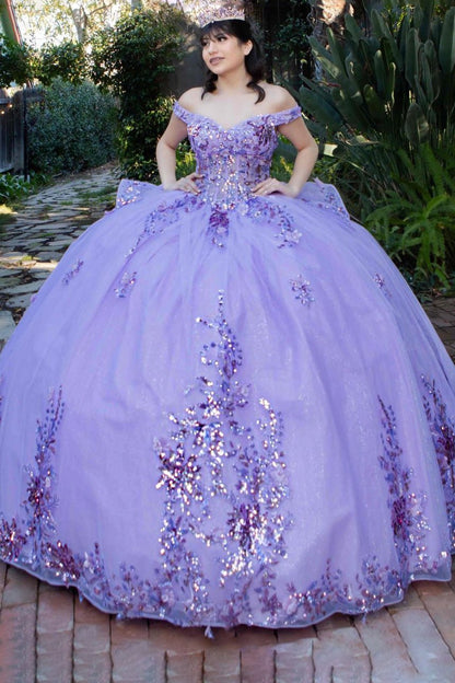 Woman in a purple sequined dress standing outdoors with greenery in the background
