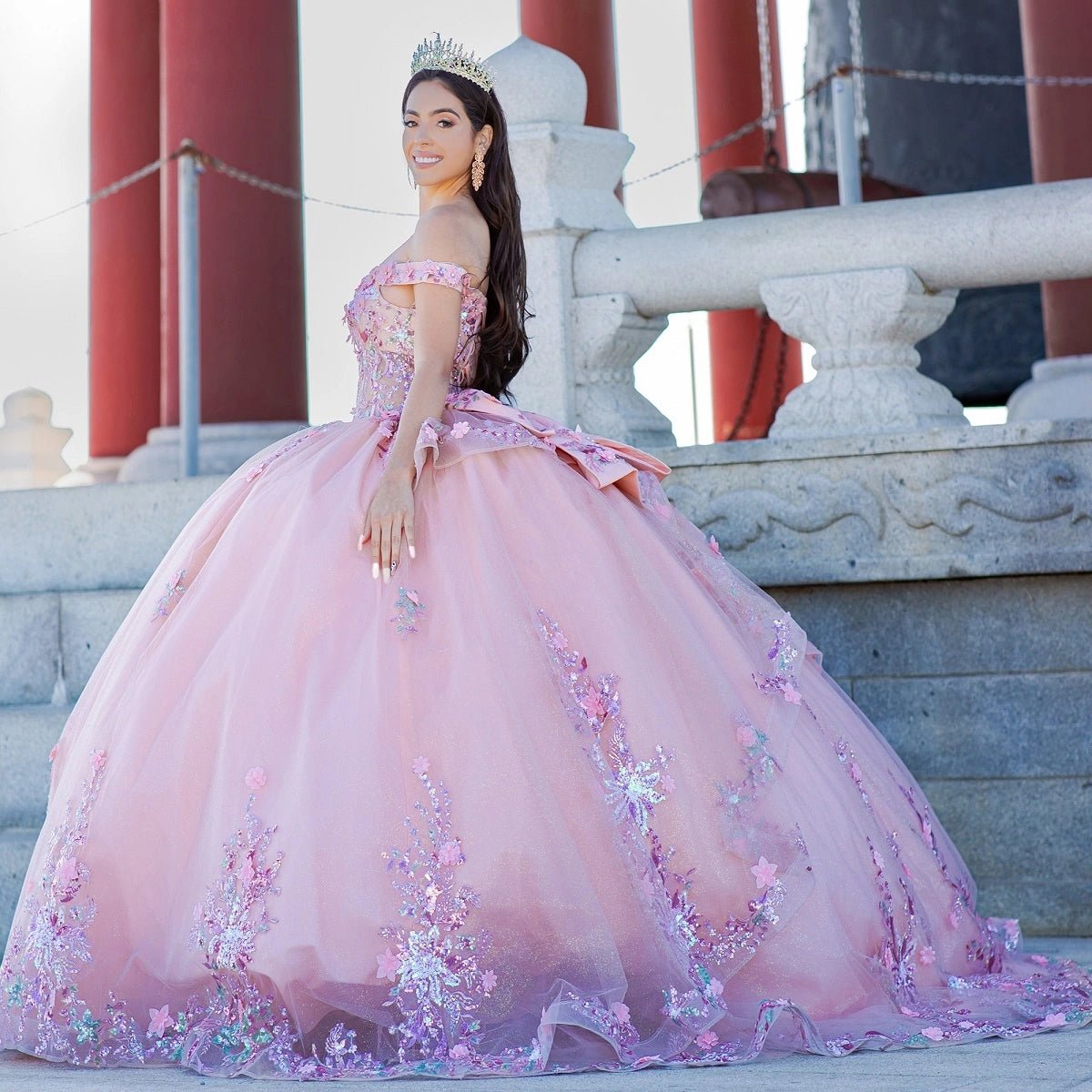 Displayed in a angled view, the Peach Blush quinceañera dress has off-shoulder neckline, floral skirt border and back bow.