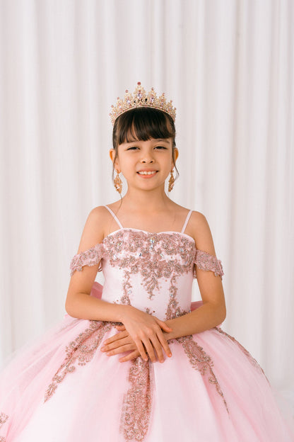 Young girl in a pink and gold dress with a tiara against a white curtain background