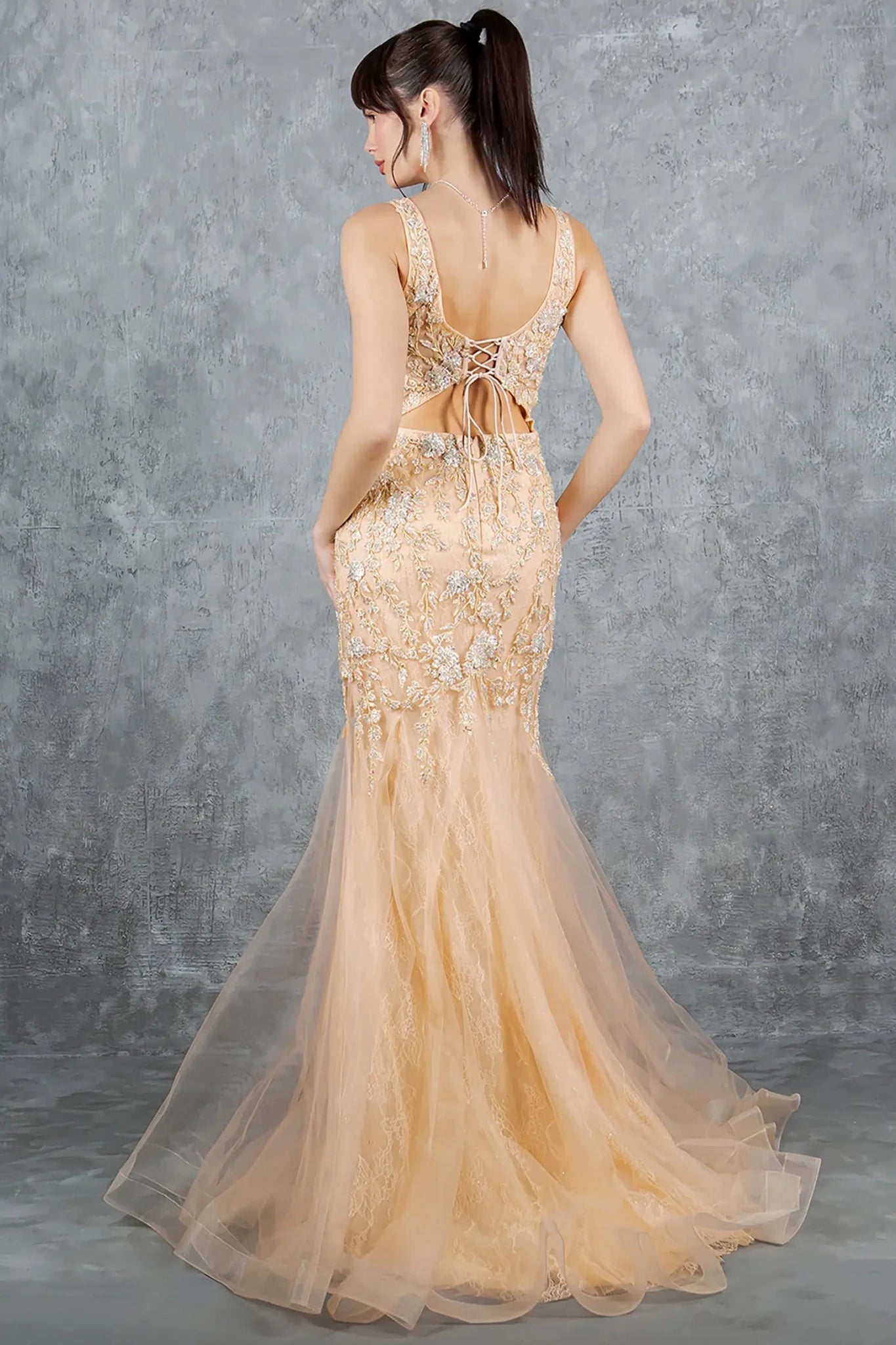 A full back view of a woman wearing a champagne formal dress with a lace-up back closure.
