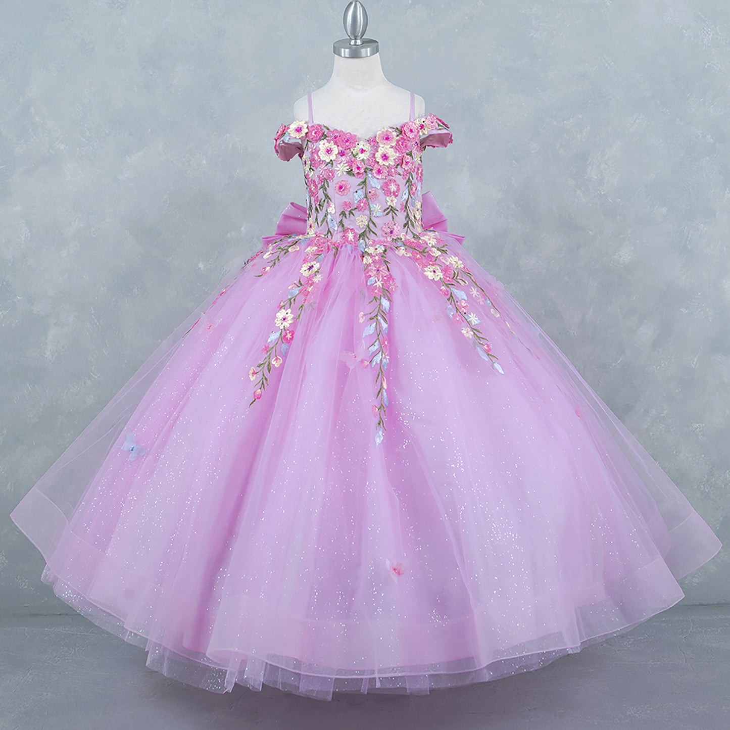 Pink side view kids mini quinceañera mini quince dress with multicolor daisy embroidery and large detachable bow.