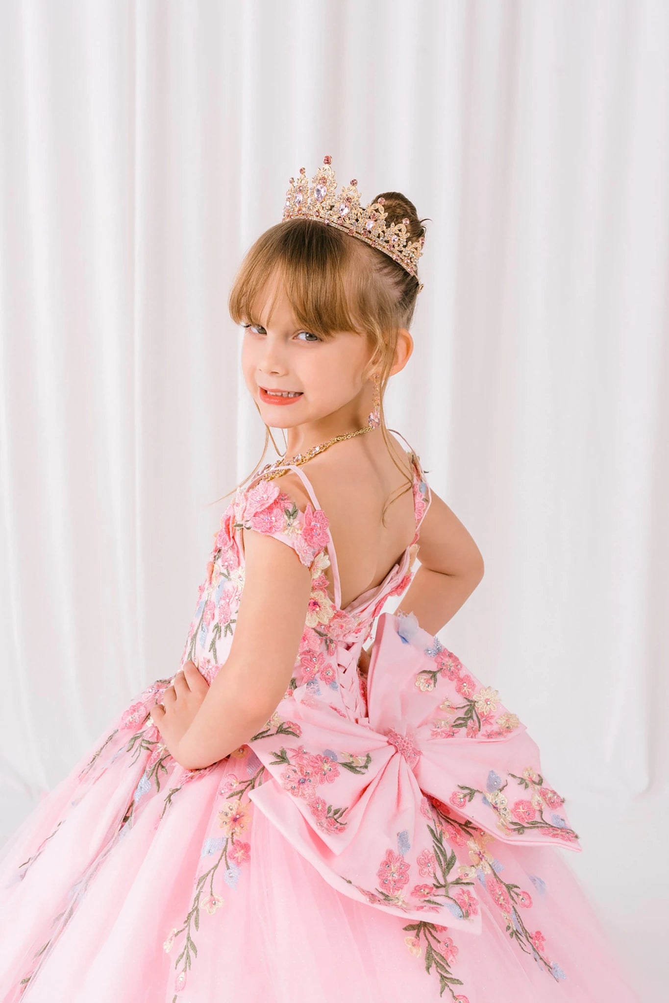Pink front view kids mini quinceañera mini quince dress with floral lace and detachable bow detail.