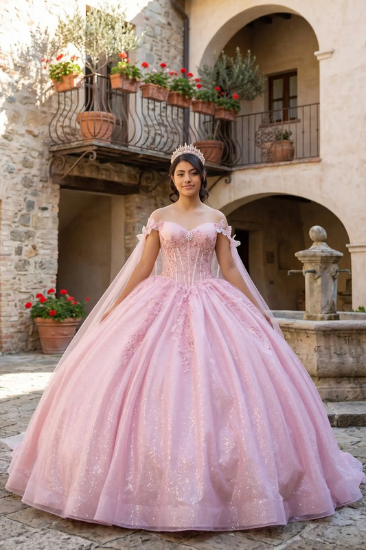 Full front view of a woman wearing rose gold quinceañera dress with glitter tulle skirt, beaded corset bodice, central brooch floral embellishments, and flowing sheer cape.