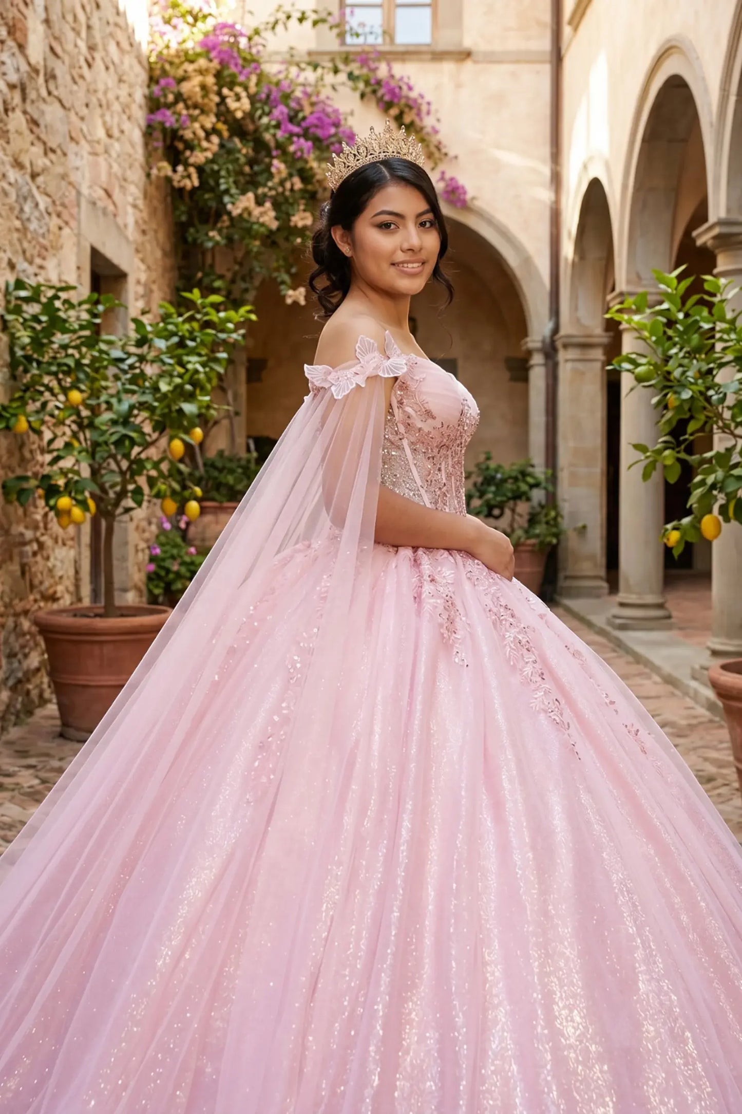 Side close-up view of a woman wearing rose gold quinceañera dress highlighting floral brooch embellishments, glitter tulle layers, and sheer cape detail.