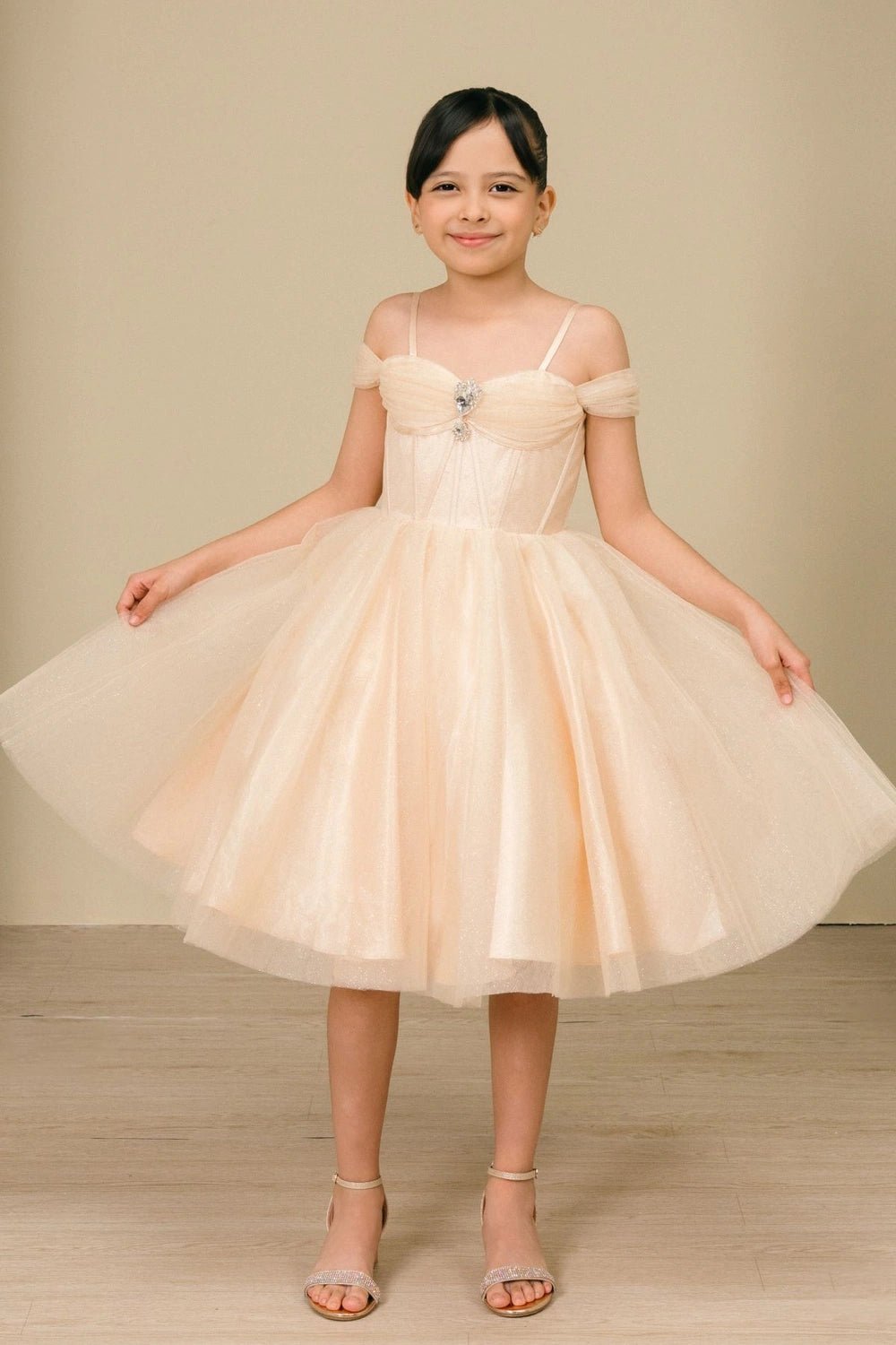 Shown in a front view, the Champagne girls formal dress has thin straps and off-shoulder bands over a full tulle skirt.