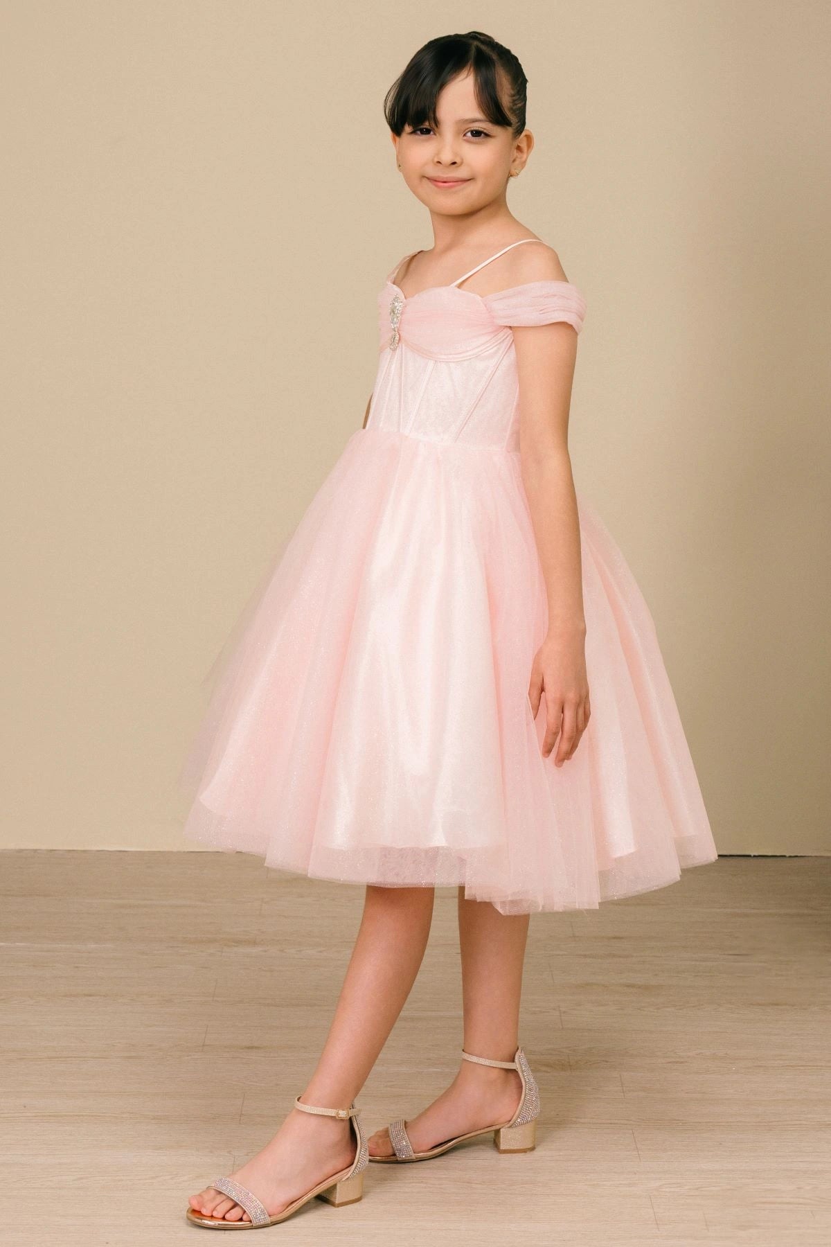 Shown in a angled view, the Pink girls formal dress has off-shoulder bands, thin straps and a pleated tulle skirt.
