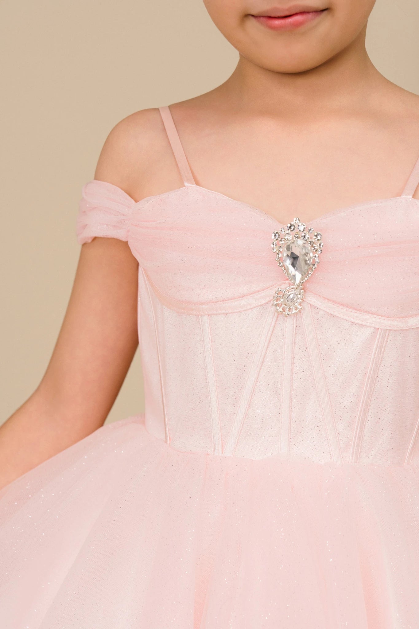 close up the top of the flower girl dress and showing the shoulder part and a big rhinestone on top of the dress.