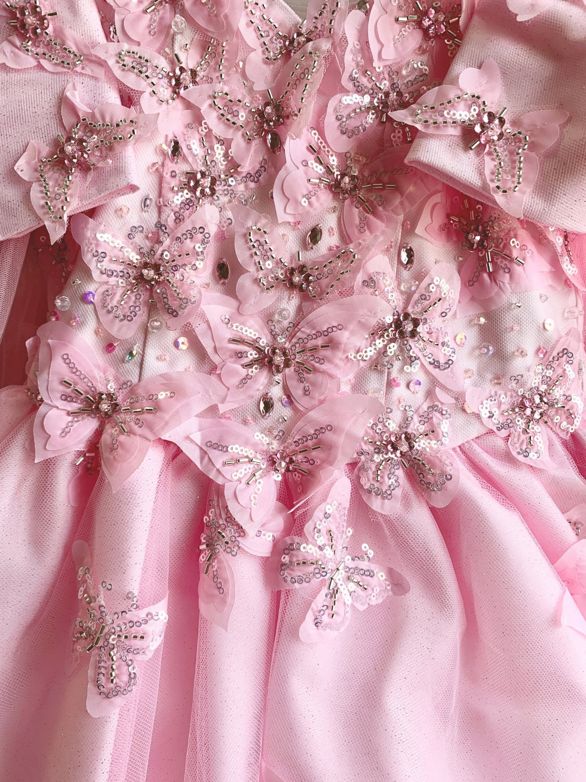 Pink fabric close-up kids mini quinceañera mini quince dress with glitter puff sleeves, butterfly applique and sequins.