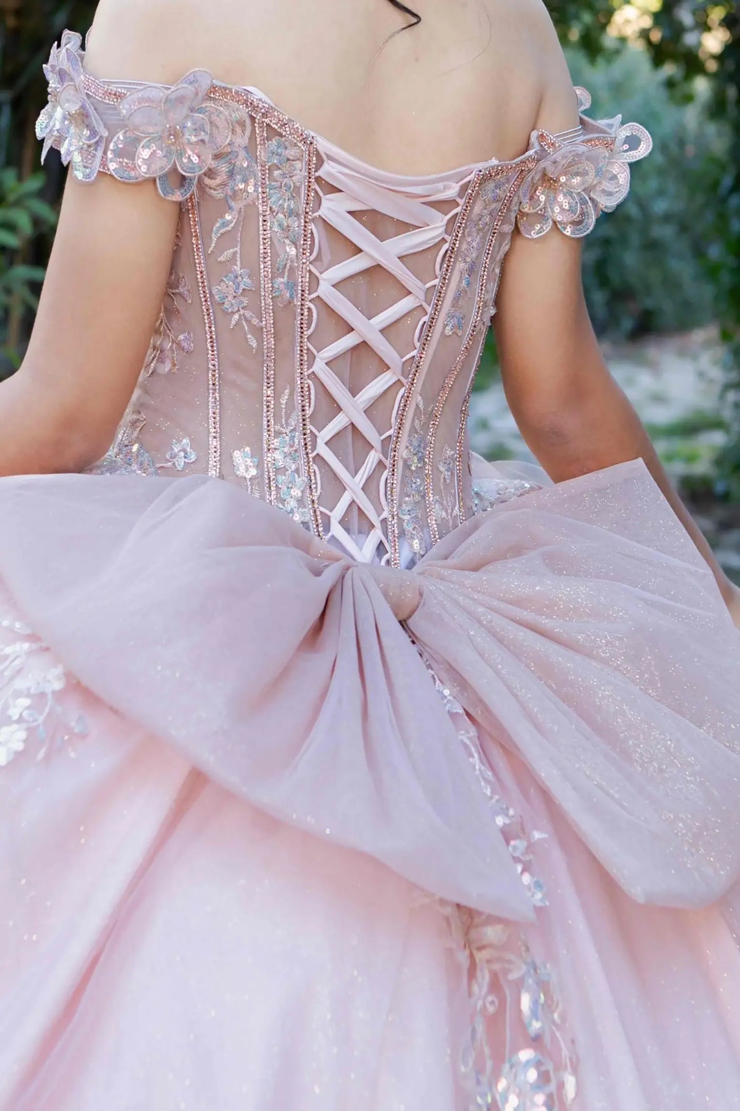 Zoomed back view of a rose gold quinceanera dress highlighting beadwork bodice, 3D floral appliques, and iridescent sequins