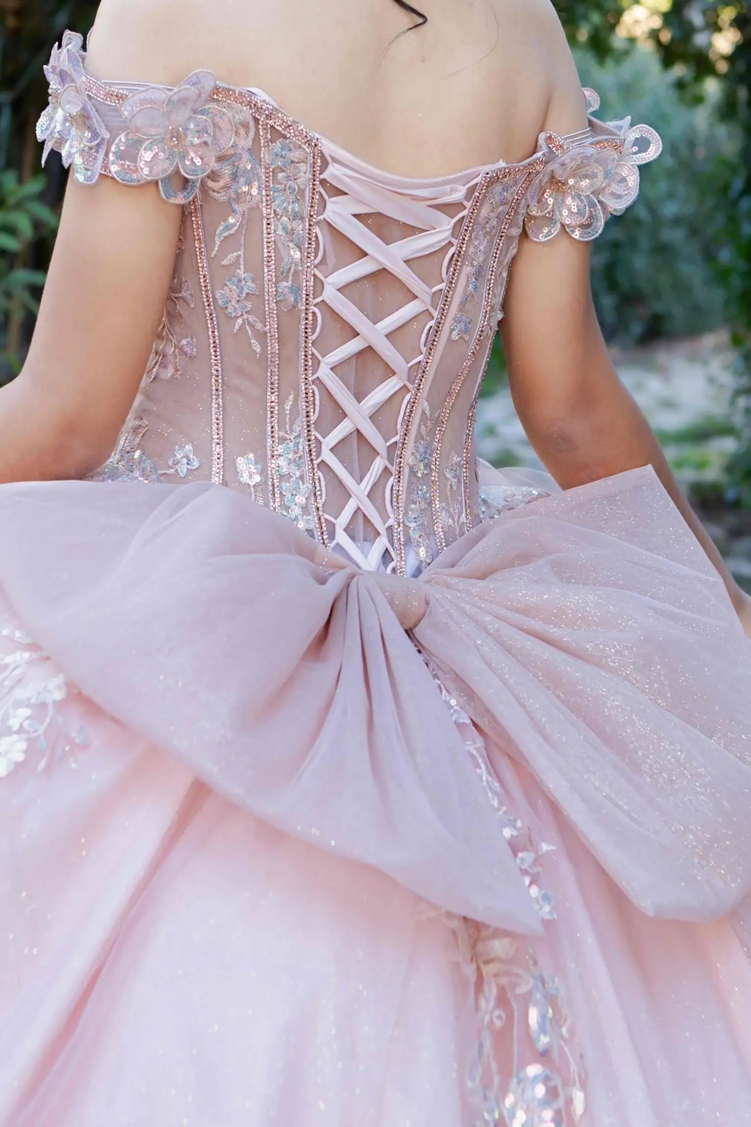 Zoomed back view of a rose gold quinceanera dress highlighting beadwork bodice, 3D floral appliques, and iridescent sequins