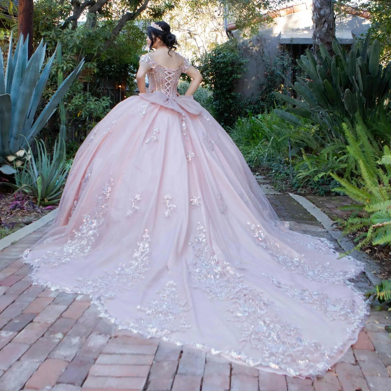 Back view of a rose gold quinceanera dress with sweetheart bodice, beadwork, 3D floral appliques, and layered shimmering tulle skirt