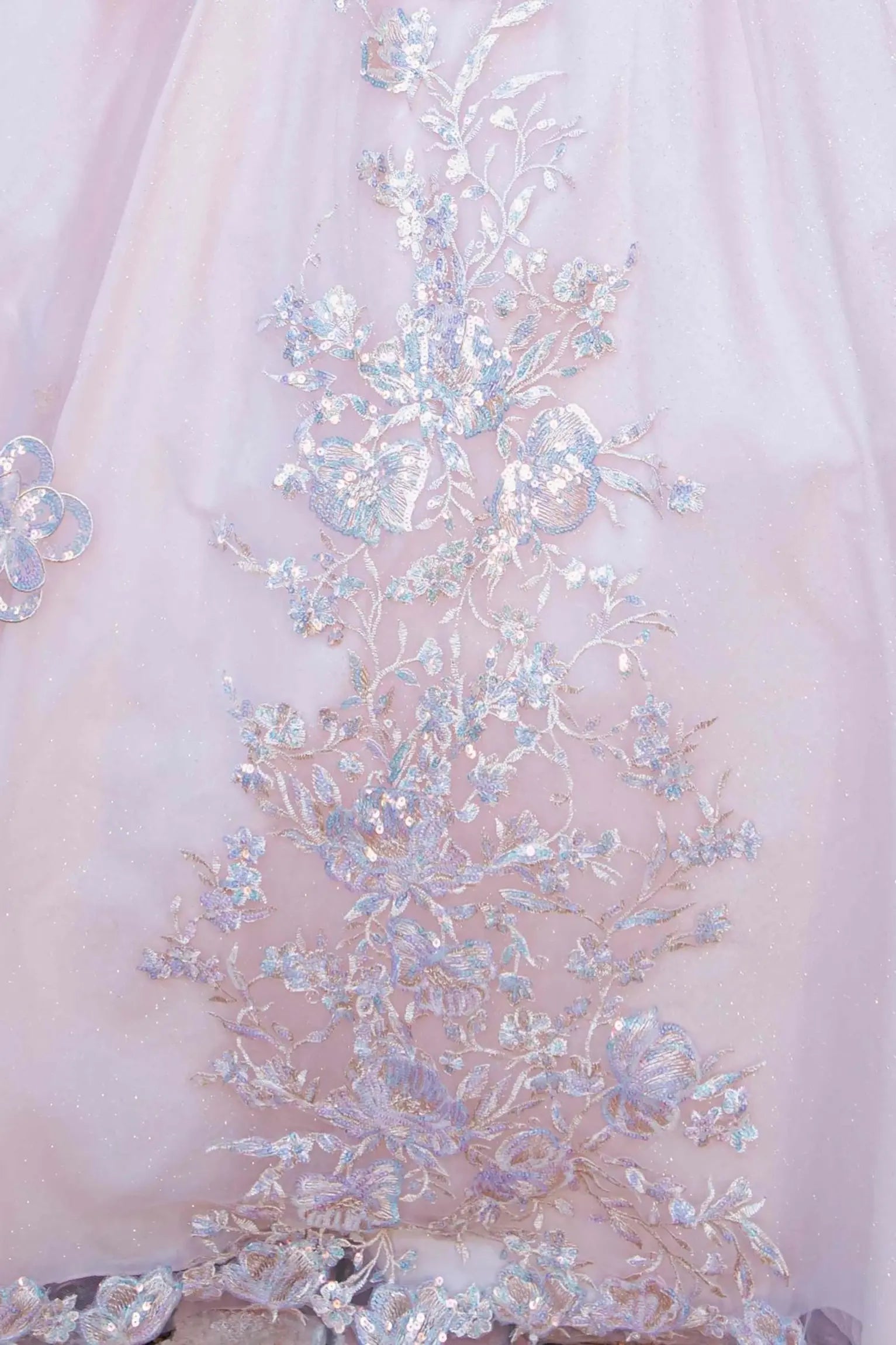 Skirt detail of a rose gold quinceanera dress with layered shimmering tulle fabric, scattered floral appliques, and chapel-length train