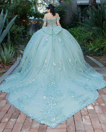Back view of a silver sage quinceanera dress with lace-up corset, voluminous tulle bow, 3D floral appliques, and chapel-length train