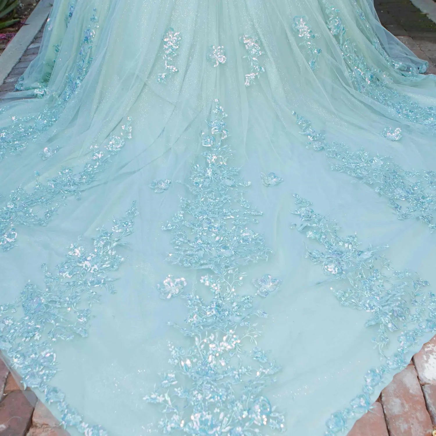 Skirt detail of a silver sage quinceanera dress with layered shimmering tulle fabric, scattered floral appliques, and chapel-length train