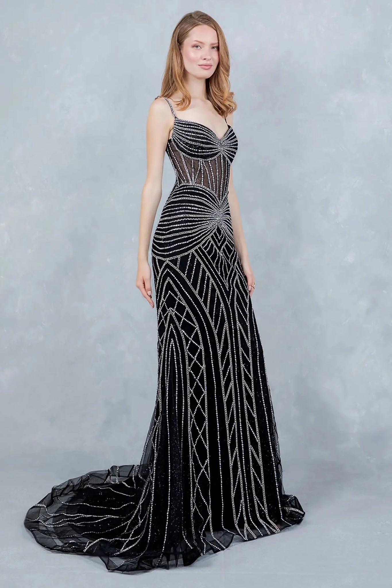 A full-length front view of a woman wearing a black mermaid dress detailed with a lace-up corset and dramatic tulle flare.