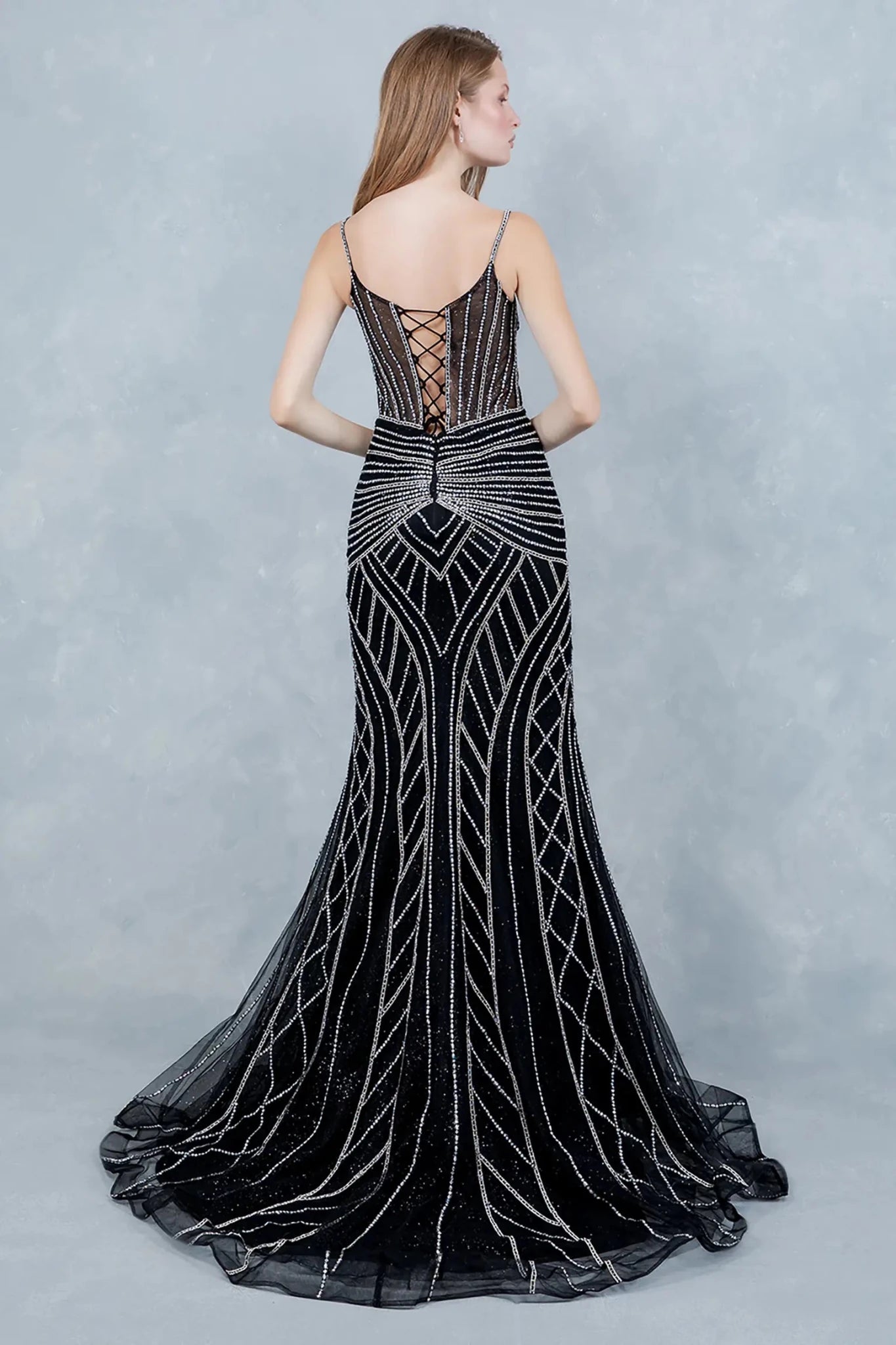 A full back view of a woman wearing a black mermaid dress with a lace-up corset and tulle flare.