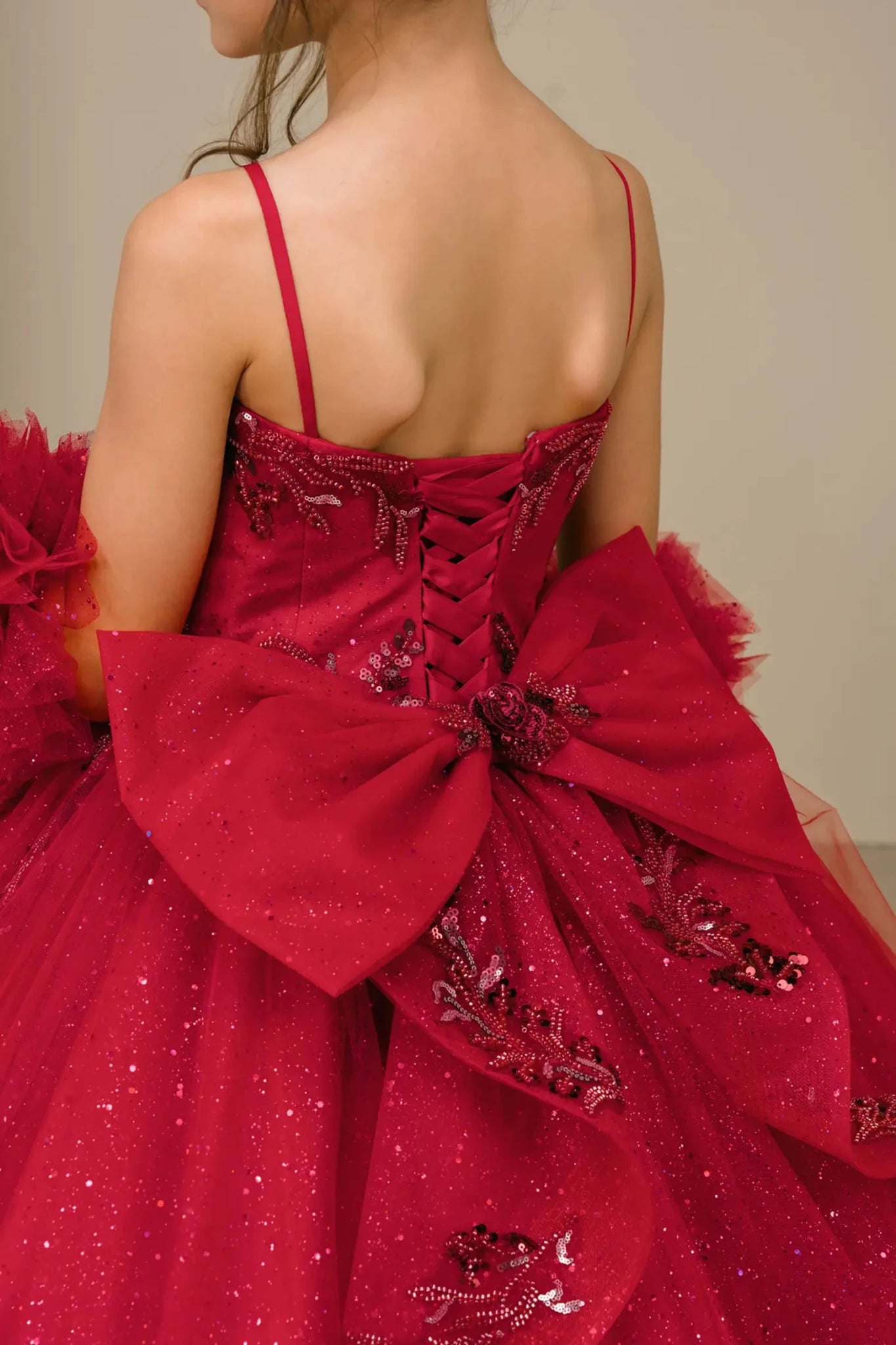 Close-up of burgundy mini quinceañera mini quince dress fabric with beaded floral appliqués, draped detailing, sparkling tulle layers, and bow accents.