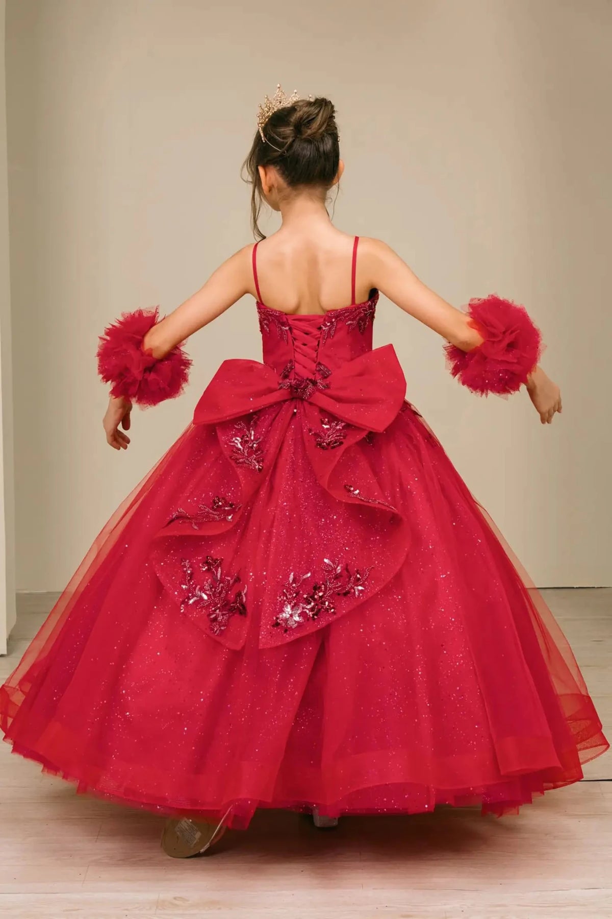 Back view of burgundy mini quinceañera mini quince dress with lace-up closure, grand layered bow, sparkling tulle skirt, and matching tulle arm cuffs.