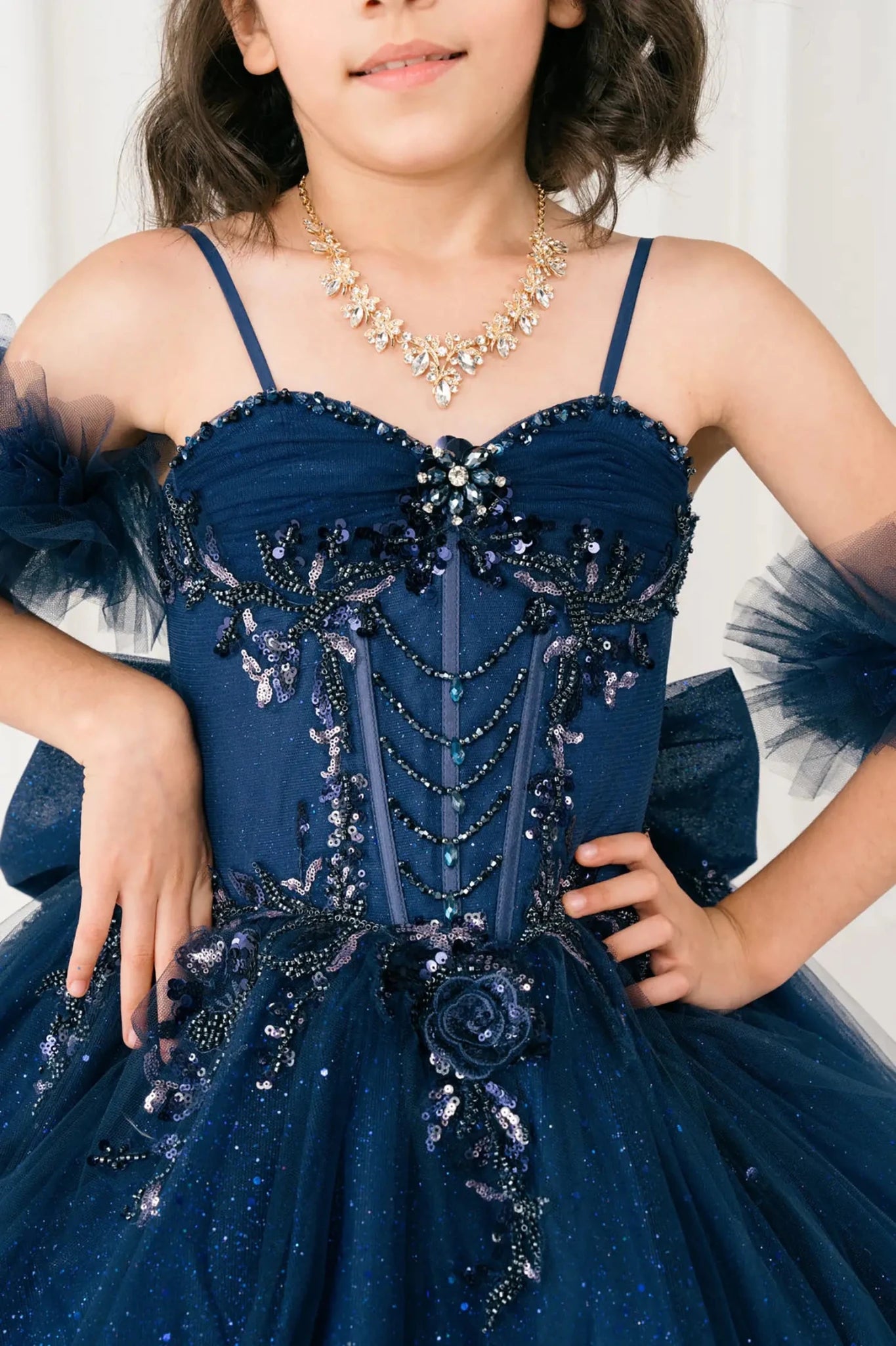 Close-up front-facing view of navy mini quinceañera mini quince dress with beaded floral appliqué bodice, draped detailing, and matching tulle arm cuffs.