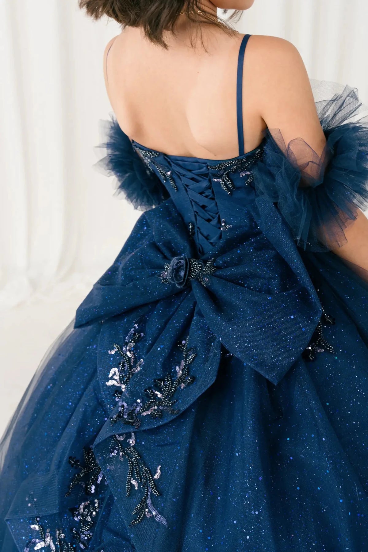 Close-up of navy mini quinceañera mini quince dress fabric with beaded floral appliqués, draped detailing, sparkling tulle layers, and bow accents.