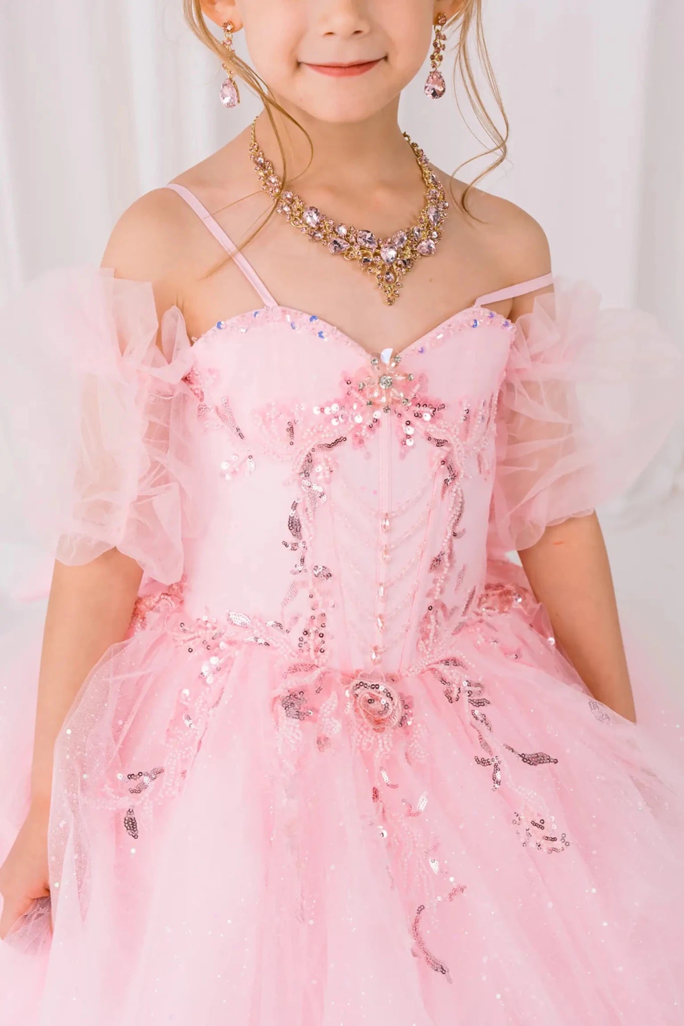 Close-up front-facing view of burgundy mini quinceañera ball gown with beaded floral appliqué bodice, draped detailing, and matching tulle arm cuffs