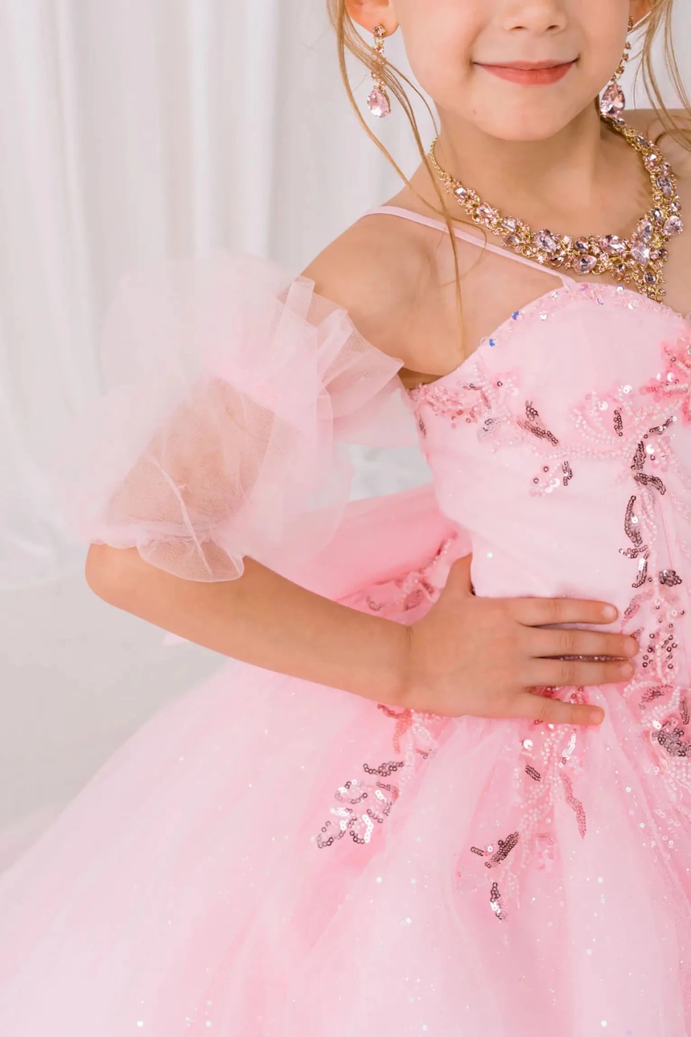 Close-up front-facing view of burgundy mini quinceañera ball gown with beaded floral appliqué bodice, draped detailing, and matching tulle arm cuffs