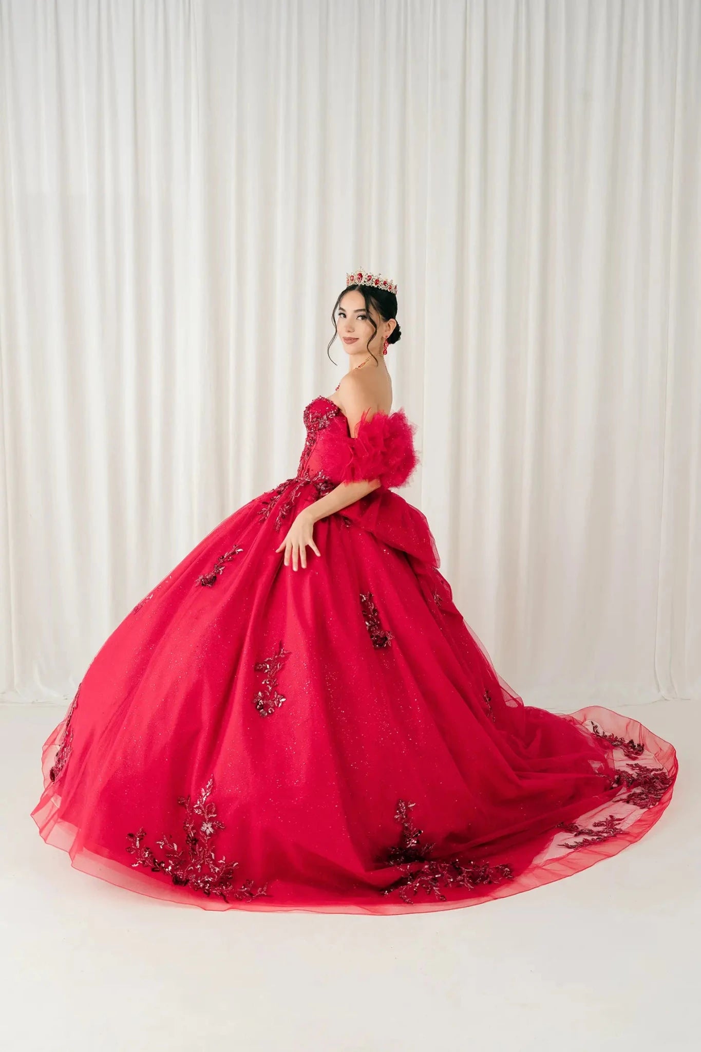 Back three-quarter view – Angled back view of red quinceañera ball gown featuring oversized bow detail and layered tulle train.