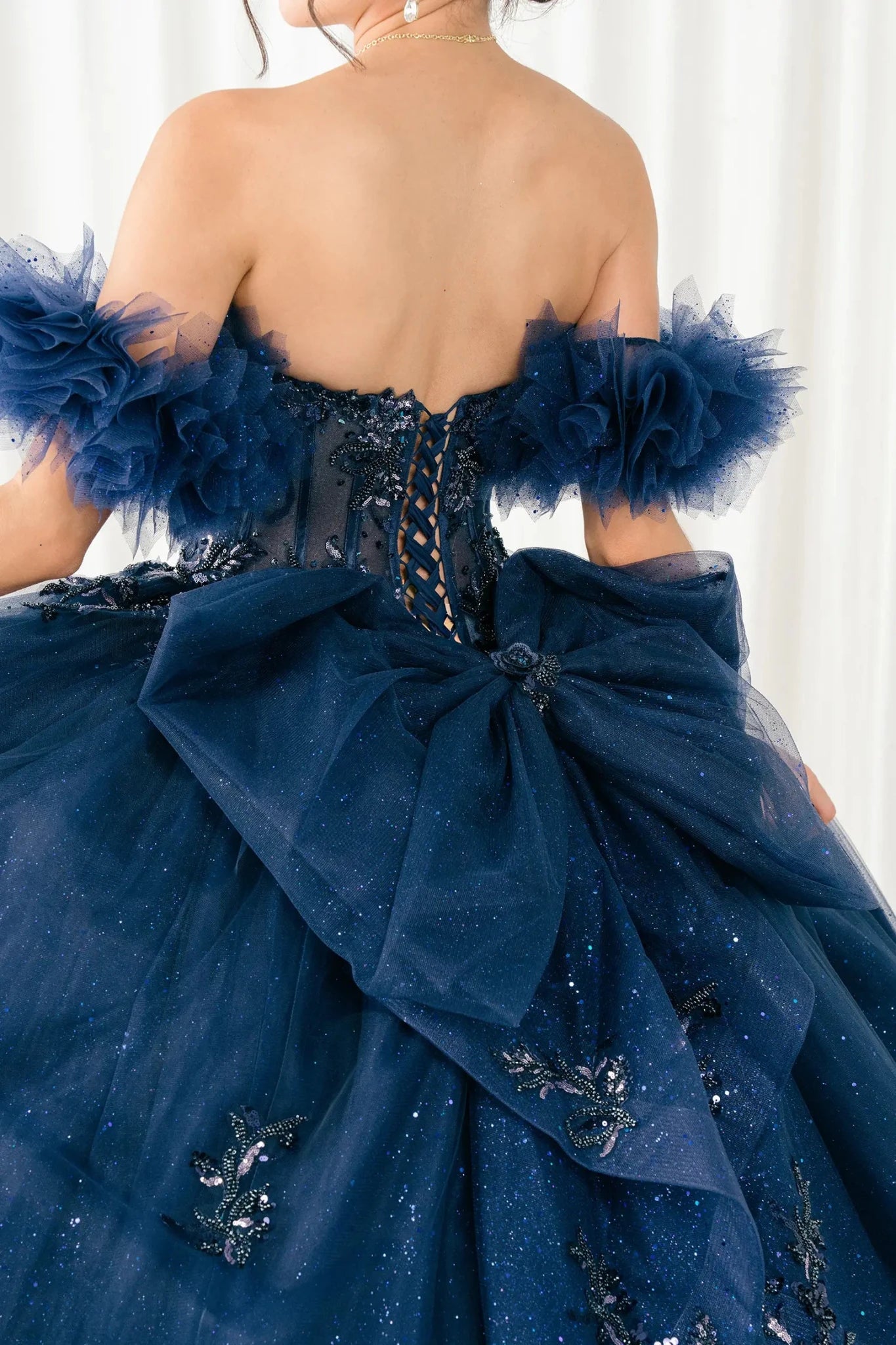 Back detail view of navy blue ball gown showing lace-up corset back and oversized bow
