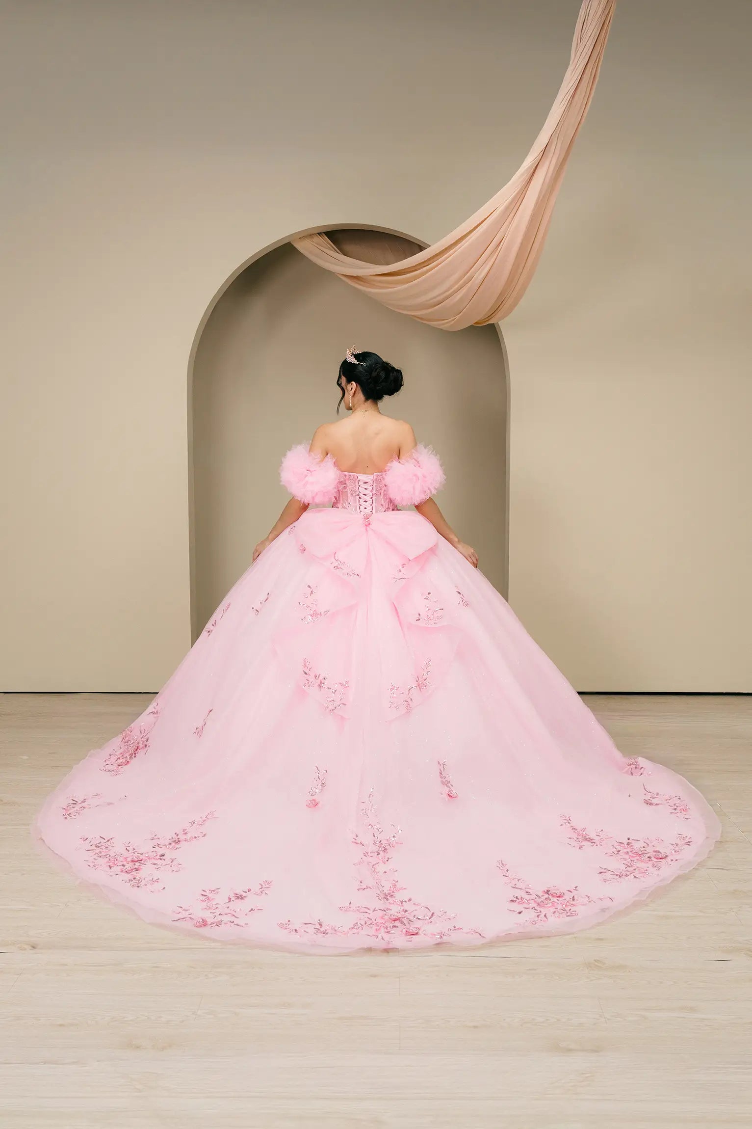 Rear full-length view of a pink quinceañera ball gown highlighting the extended train and embroidered hem