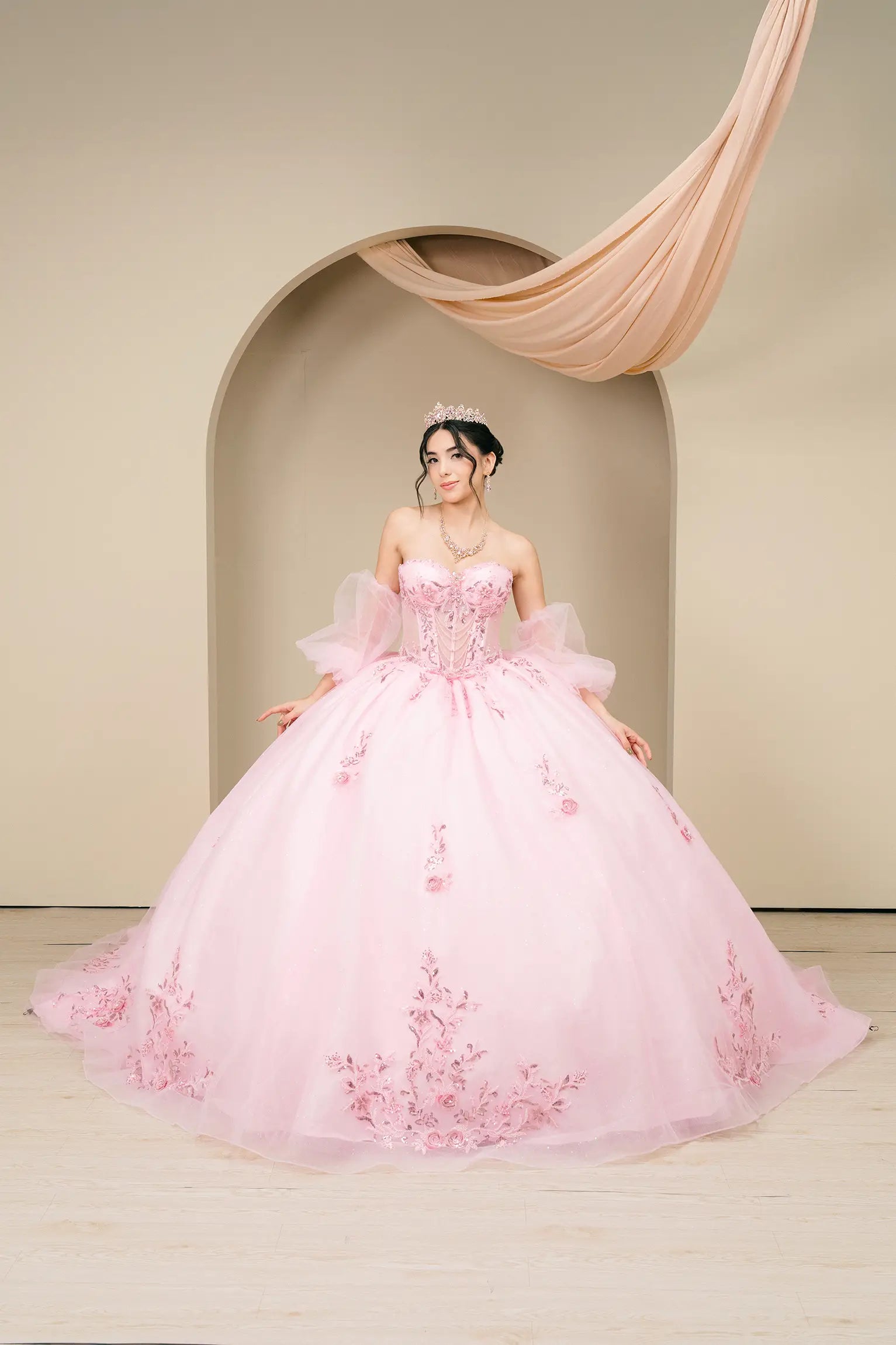 Front full-length view of a pink off-shoulder quinceañera ball gown with fitted corset and voluminous skirt