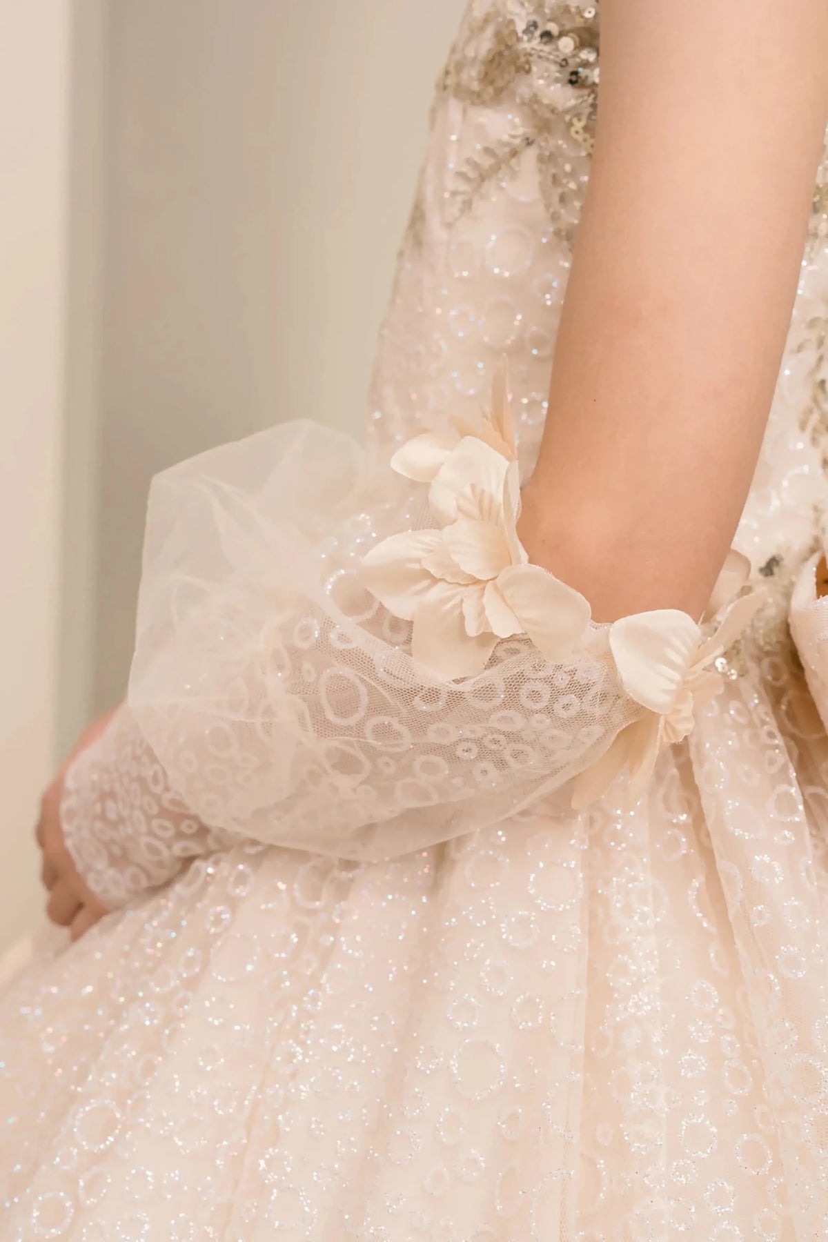 Side close up view of Champagne mini quince mini quince dress with glitter floral embroidered bodice, and sheer lace gloves.