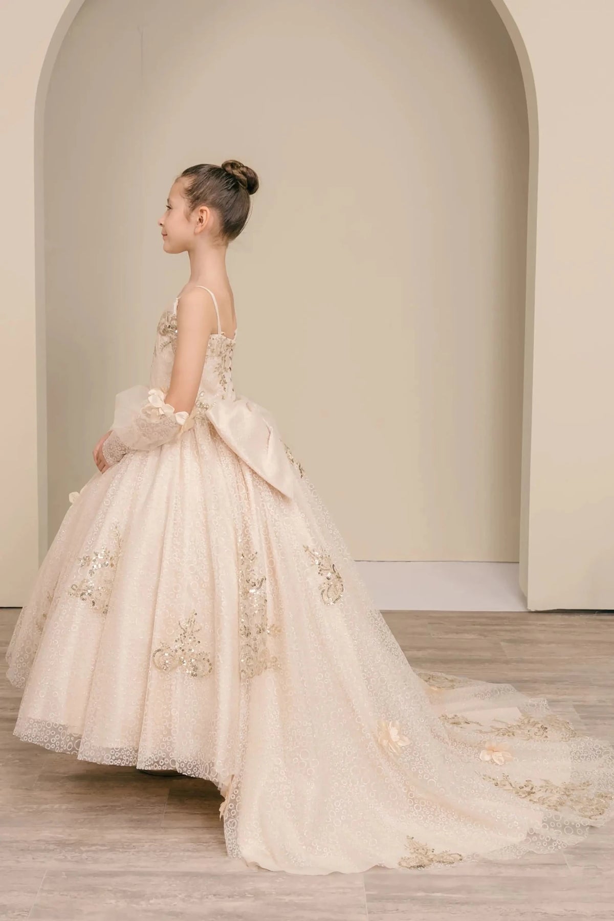 Side full-length view of Champagne mini quince mini quince dress with glitter floral embroidered bodice, full skirt, lace up back, oversized bow, and sheer lace gloves.