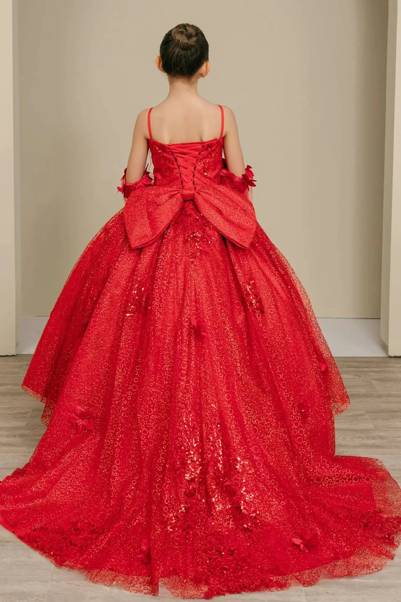 Back view of a red kids quinceañera dress with layered tulle skirt, lace-up corset closure, and floral embroidered accents.