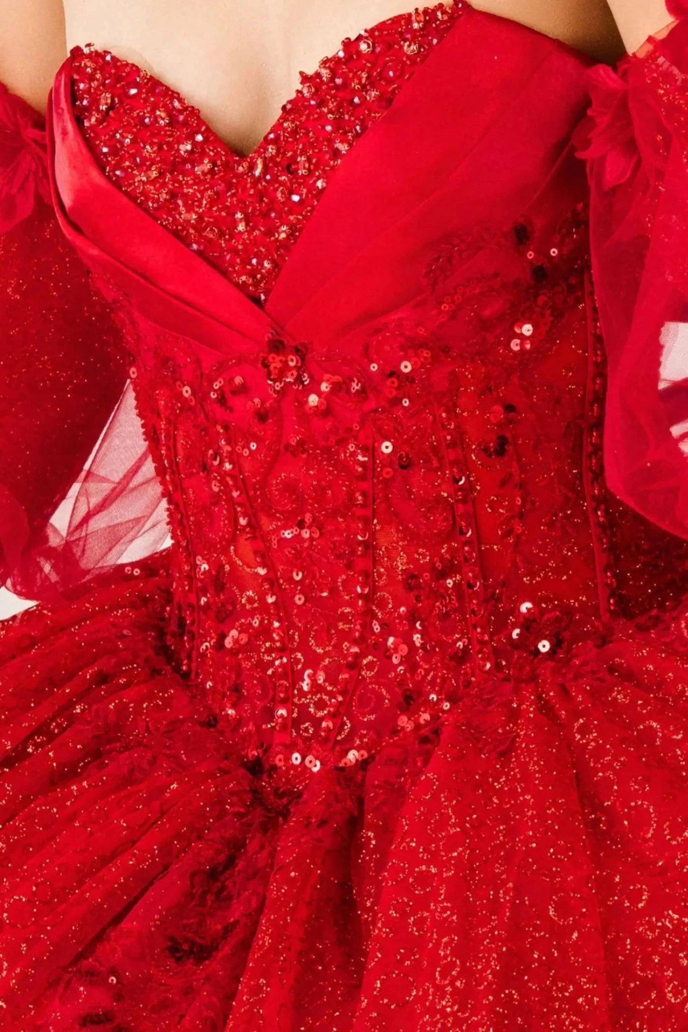 Bodice close-up of a red kids quinceañera dress showing glitter floral embroidery, sequins, and beadwork details.
