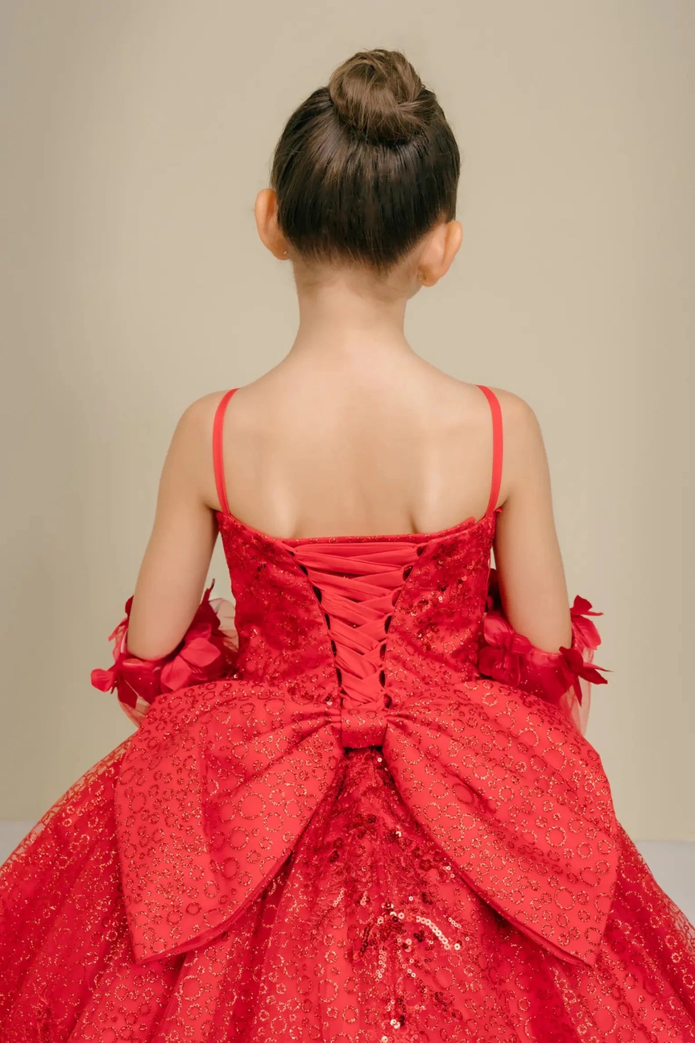 Bodice back close-up of a red kids quinceañera dress with floral embroidery, sequins, and lace-up corset detail.