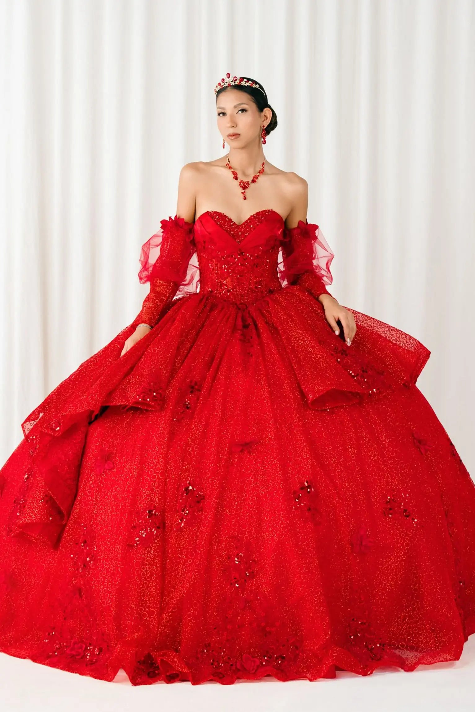 Full front view of a woman wearing red quinceañera dress with glitter tulle skirt, floral applique bodice, and detachable sheer tulle sleeves.
