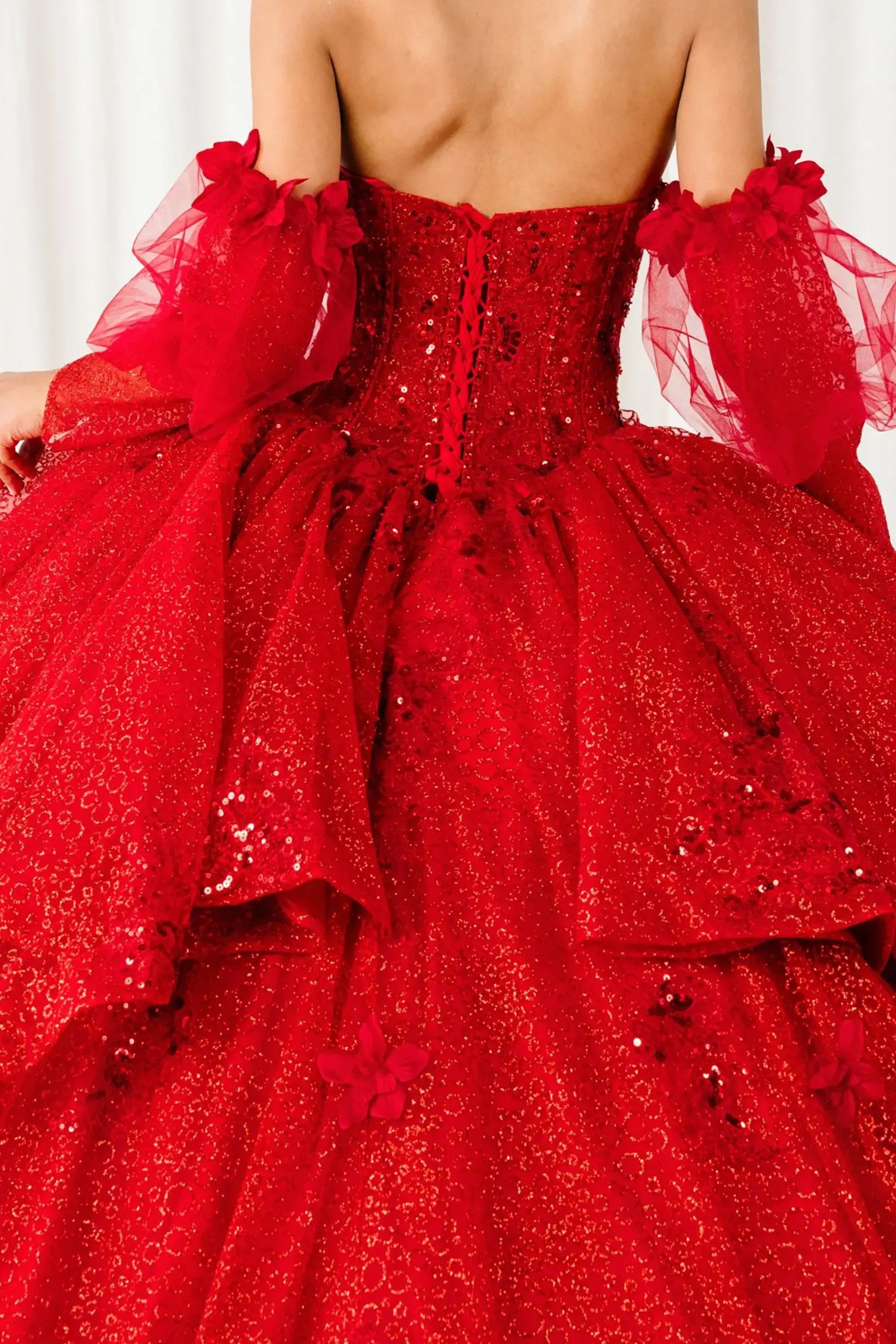 Back view of a red quinceañera dress with voluminous glitter tulle skirt, lace-up corset closure, and floral applique embellishments.